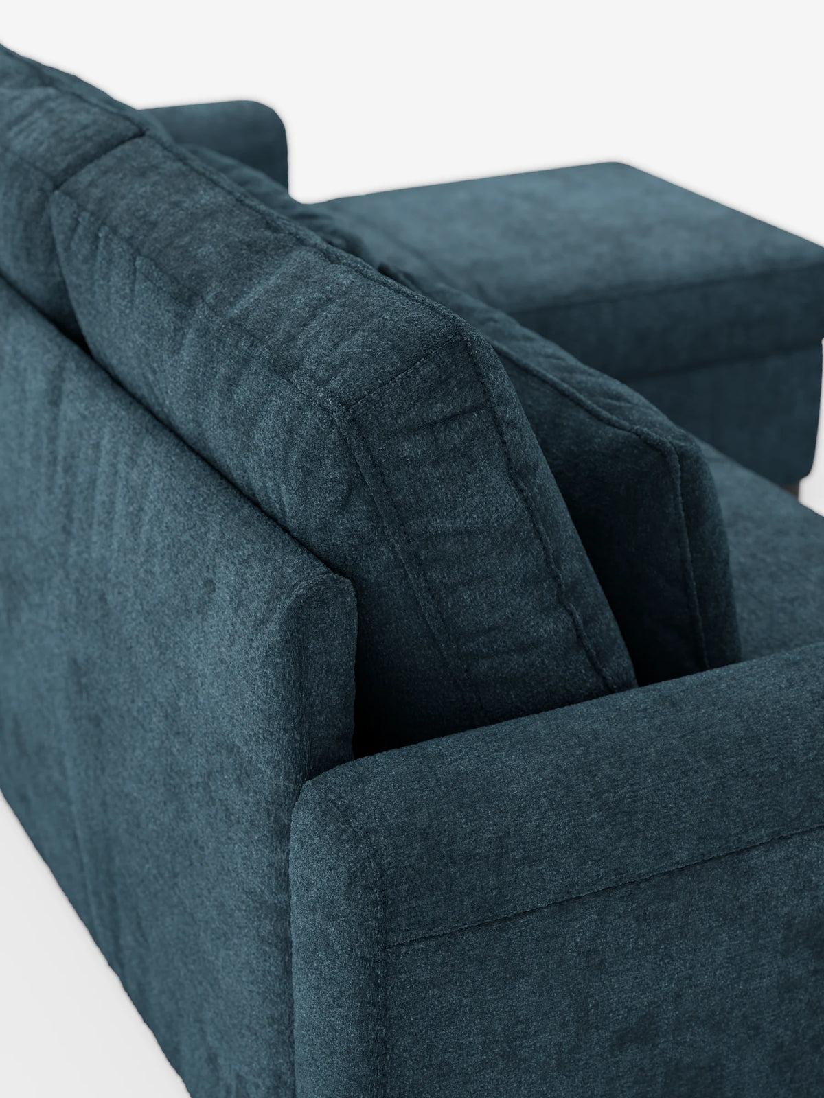 Un divano letto Ottaviano blu scuro con letto estraibile – penisola reversibile e contenitore in tessuto materico smacchiabile, con chaise longue, è posizionato su uno sfondo bianco a tinta unita, mettendo in risalto il tessuto materico e il design angolare.