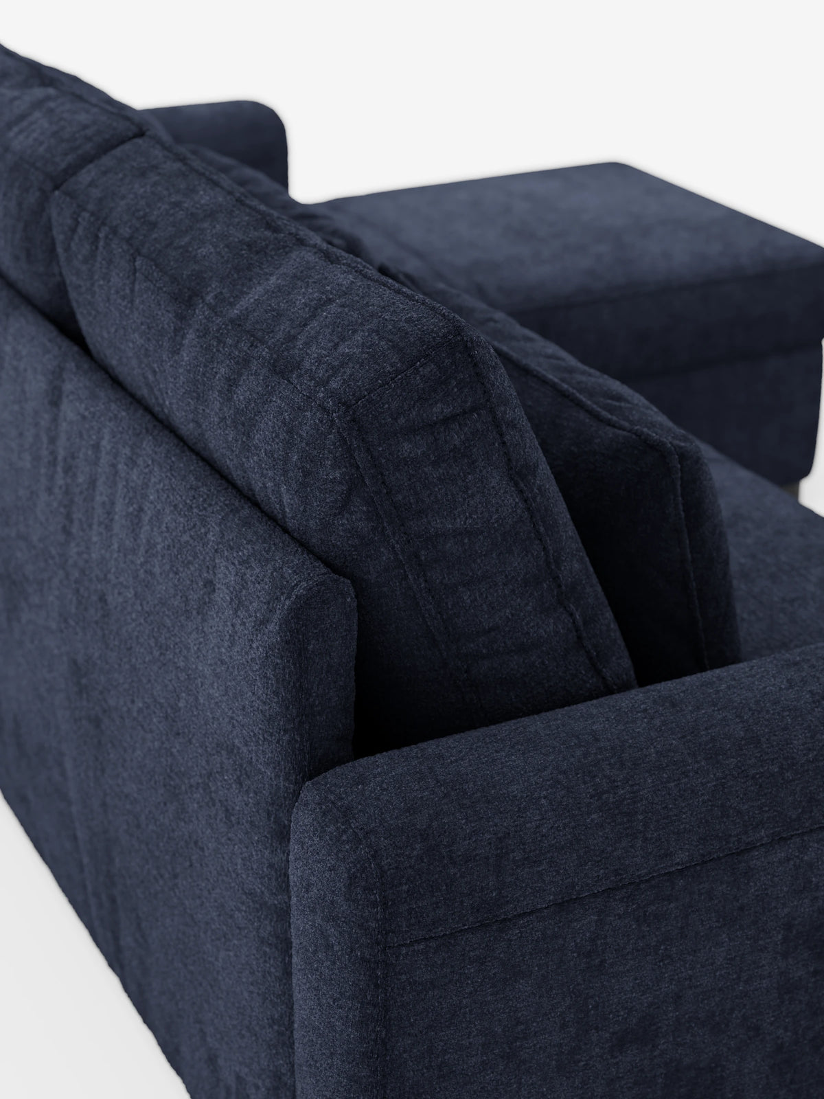 Vista dall'alto del divano letto Ottaviano con letto estraibile - penisola reversibile e contenitore in tessuto materico smacchiabile: un divano componibile blu scuro con morbidi cuscini dello schienale e una chaise longue rettangolare a forma di penisola su sfondo bianco.