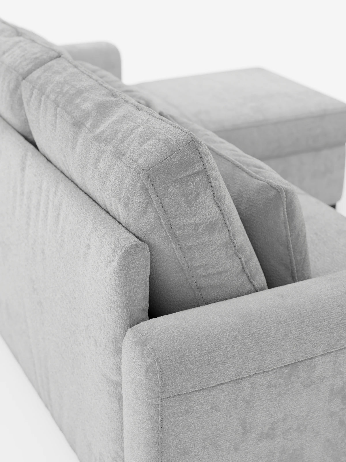 Un divano letto Ottaviano grigio chiaro con letto estraibile, penisola reversibile e contenitore, realizzato in tessuto materico smacchiabile, visto da dietro e di lato, che mostra il tessuto testurizzato sui cuscini squadrati e un ampio bracciolo su sfondo bianco.