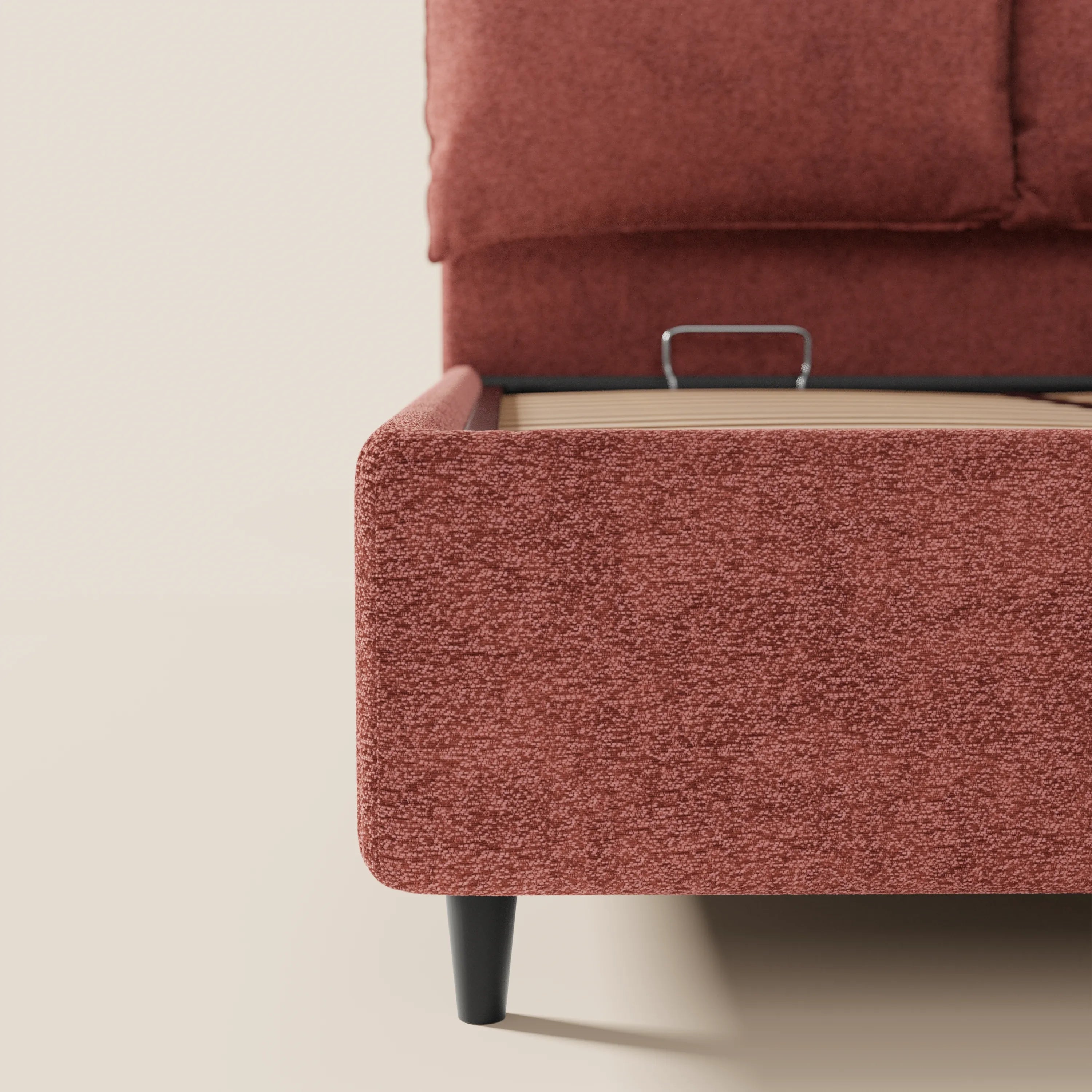 Un primo piano mostra il letto imbottito ZAYRON con contenitore di Letti.store, caratterizzato da un tessuto rosso testurizzato certificato Oeko-Tex®, gambe affusolate nere e morbidi cuscini regolabili. Lo sfondo semplice mette in risalto il suo design moderno e il colore vivace.