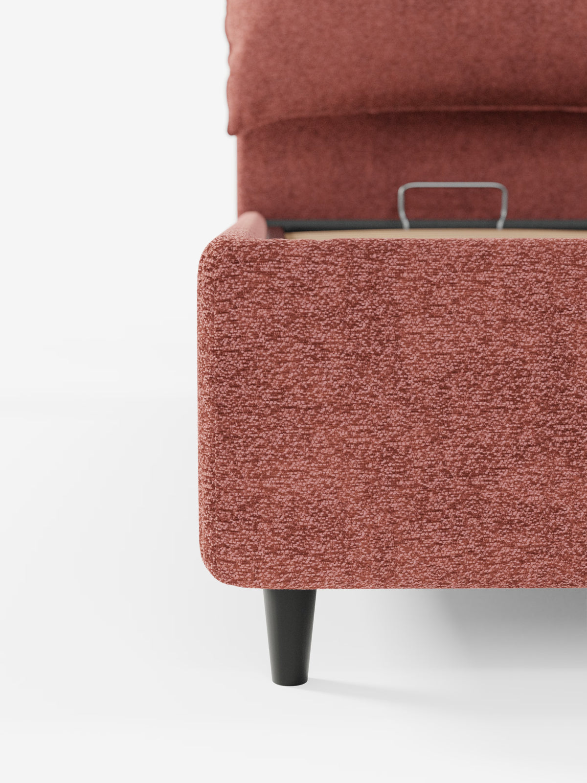 Primo piano del letto imbottito ZAYRON con contenitore e morbidi cuscini regolabili di Letti.store, che mette in risalto il rivestimento testurizzato color ruggine certificato Oeko-Tex® e l’elegante gamba nera. L’immagine ritrae l’angolo inferiore con una maniglia metallica visibile sopra la base del letto, che ne sottolinea la pratica funzionalità di contenimento, il tutto su uno sfondo bianco a tinta unita.