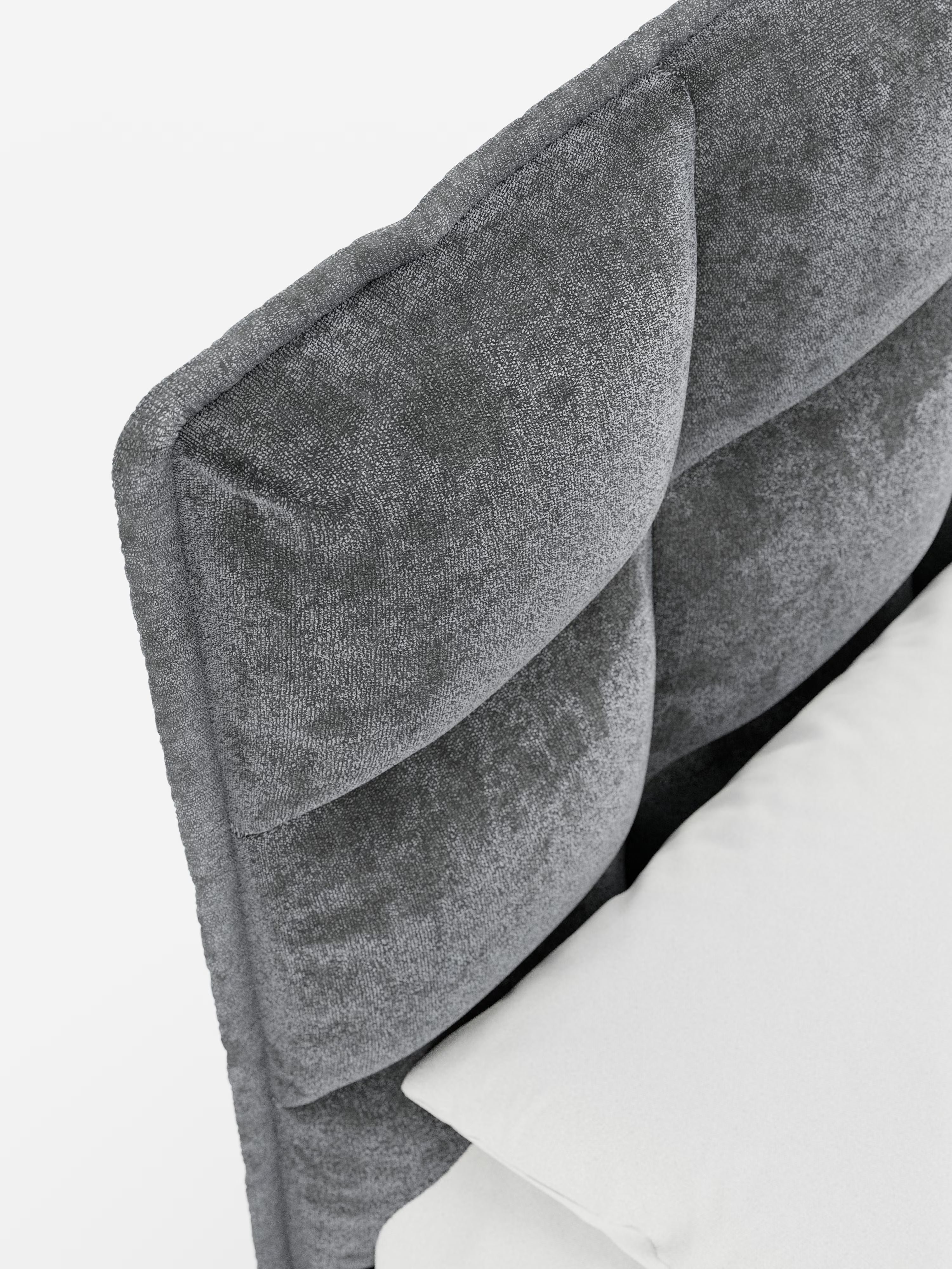 Primo piano del letto imbottito AURO con contenitore e testiera capitonné alta in ciniglia Oeko-Tex® di Letti.store, che mette in risalto la testiera grigia trapuntata con una morbida finitura vellutata in ciniglia e eleganti dettagli capitonné. La testiera alta presenta ampie sezioni rettangolari imbottite che richiamano lo stile classico. Un cuscino bianco e un materasso fanno capolino in basso a destra su uno sfondo bianco a tinta unita, sottolineando il fascino raffinato di questo letto imbottito con