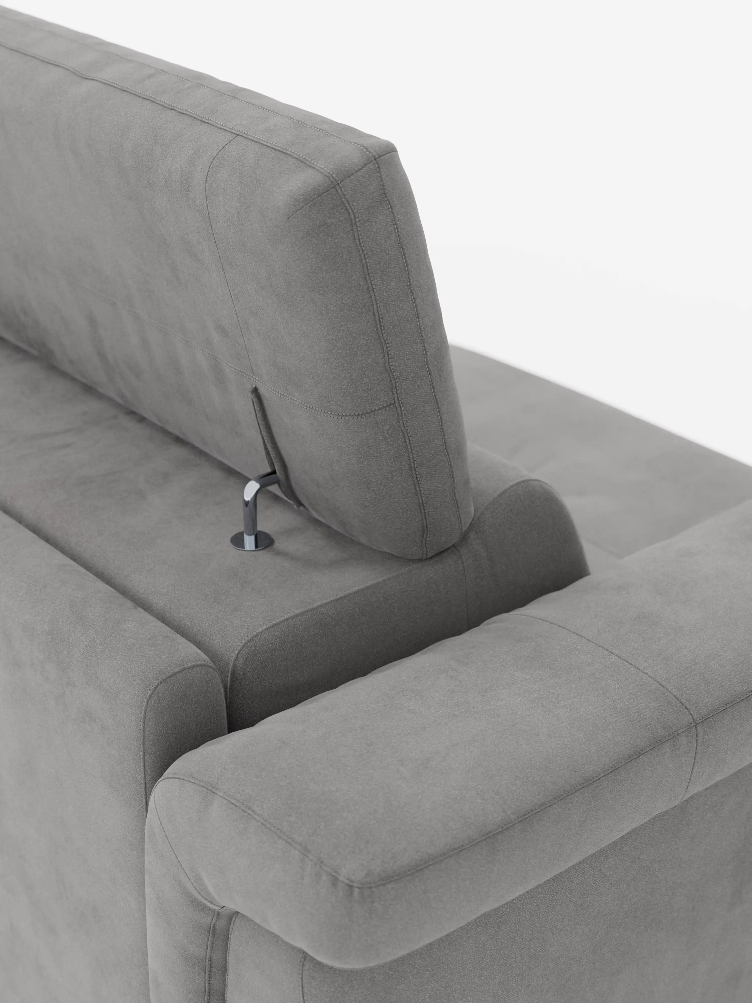 Primo piano del divano letto di design Capri di Divani.Store, caratterizzato da un moderno angolo grigio con poggiatesta reclinabili fissati tramite eleganti aste metalliche. Il raffinato tessuto effetto velluto smacchiabile T30 presenta una morbida consistenza simile alla pelle scamosciata ed è caratterizzato da cuciture lisce e pulite che incarnano la manifattura italiana. Lo sfondo bianco a tinta unita mette in risalto gli eleganti dettagli di design del divano e i suoi caratteristici piedini alti.
