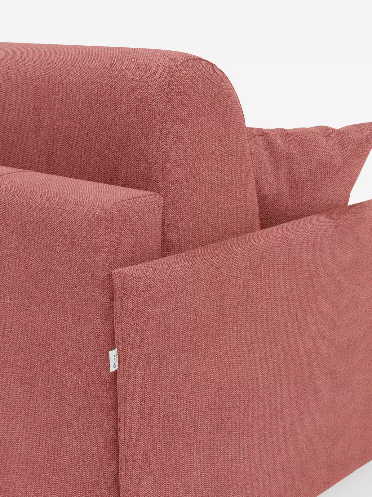 Primo piano del divano letto matrimoniale sfoderabile Evans di Divani.Store, un moderno divano letto salvaspazio rivestito in tessuto rosso opaco a trama rigata (T23). L'immagine mette in risalto il bracciolo sinistro con una piccola etichetta in tessuto bianco, lo schienale spesso e un cuscino coordinato. Lo sfondo è bianco a tinta unita.