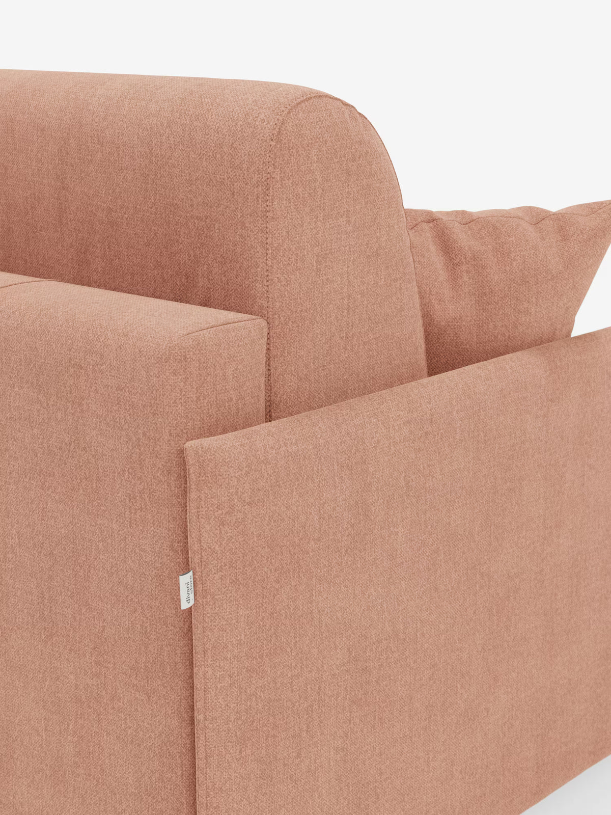 Primo piano del divano letto matrimoniale sfoderabile Evans di Divani.Store: il suo design compatto e moderno è rivestito in tessuto T23 color terracotta tenue, resistente alle macchie. L’immagine mette in risalto i braccioli, lo schienale e un cuscino di seduta del divano, accompagnato da un cuscino coordinato. Una piccola etichetta in tessuto bianco è applicata sul lato, il tutto su uno sfondo bianco a tinta unita.