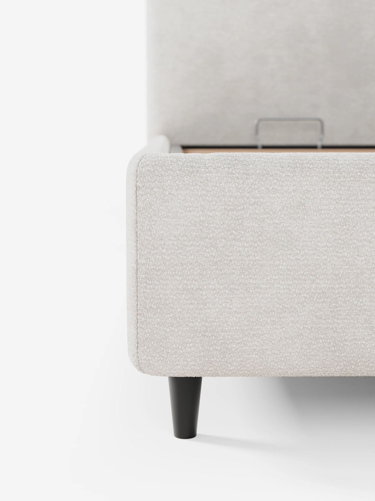 Un primo piano del letto imbottito KAELOS “minimal”, un letto rivestito in tessuto beige chiaro con finitura testurizzata, caratterizzato da una testiera arrotondata, una base rialzata su una sottile gamba nera e una maniglia in metallo all'interno del vano contenitore.