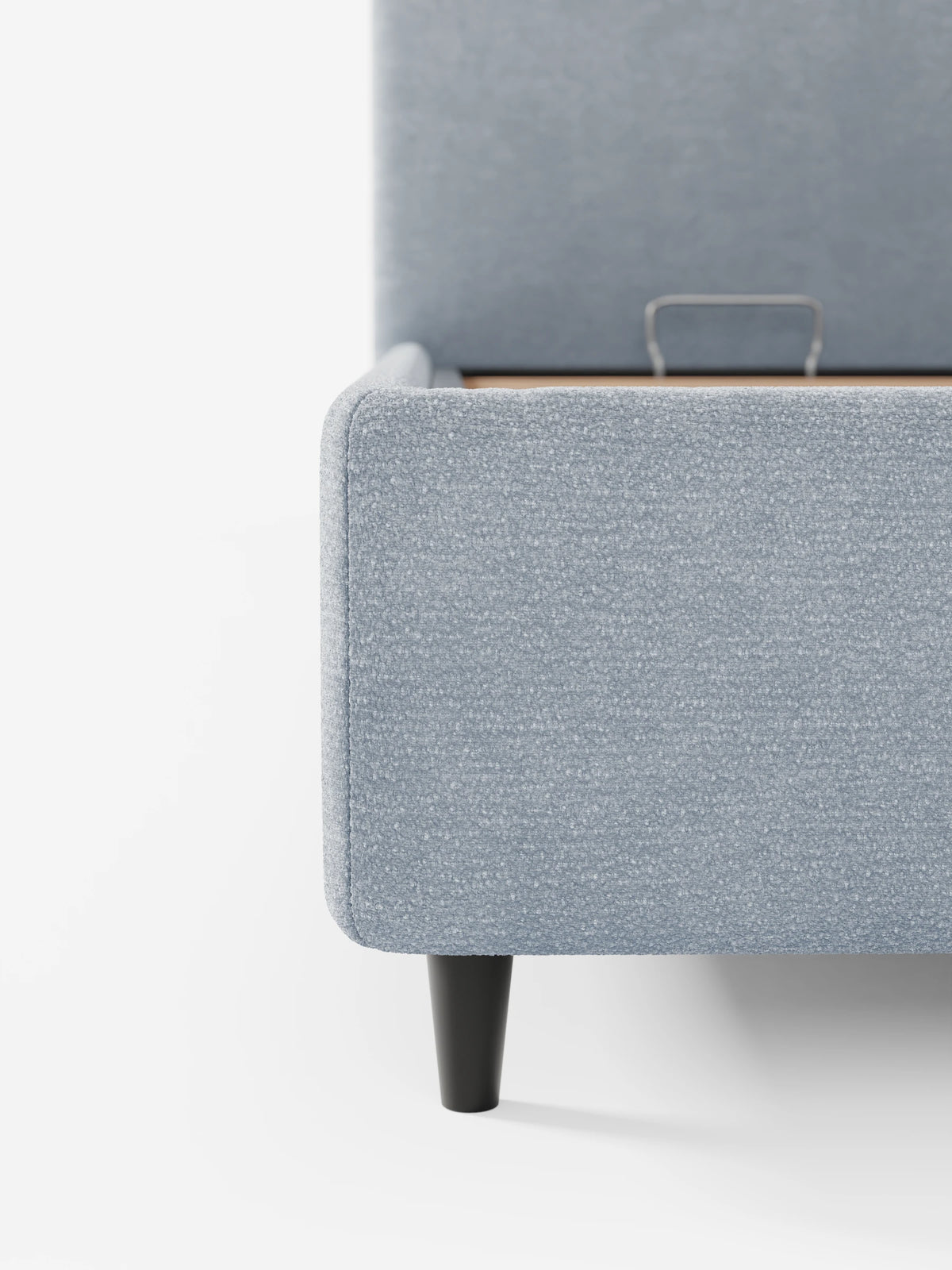 Un primo piano di un divano KAELOS Letto Minimal imbottito di colore azzurro: vano contenitore, piedini alti e testiera arrotondata in tessuto ciniglia, con una testiera arrotondata, tessuto testurizzato, una maniglia metallica per l'apertura del vano contenitore e piedini corti, scuri e affusolati.