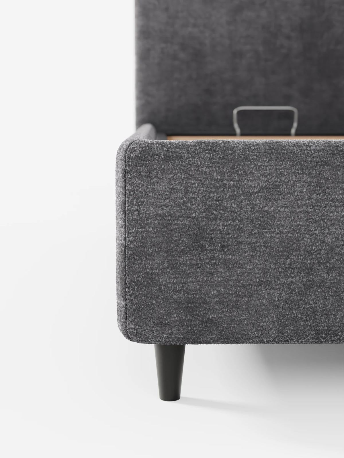 Un primo piano di un divano angolare KAELOS Letto Minimal imbottito, color grigio antracite, con finitura testurizzata, caratterizzato da una gamba alta e affusolata di colore nero e da una maniglia in metallo alla base della testiera, su sfondo bianco.