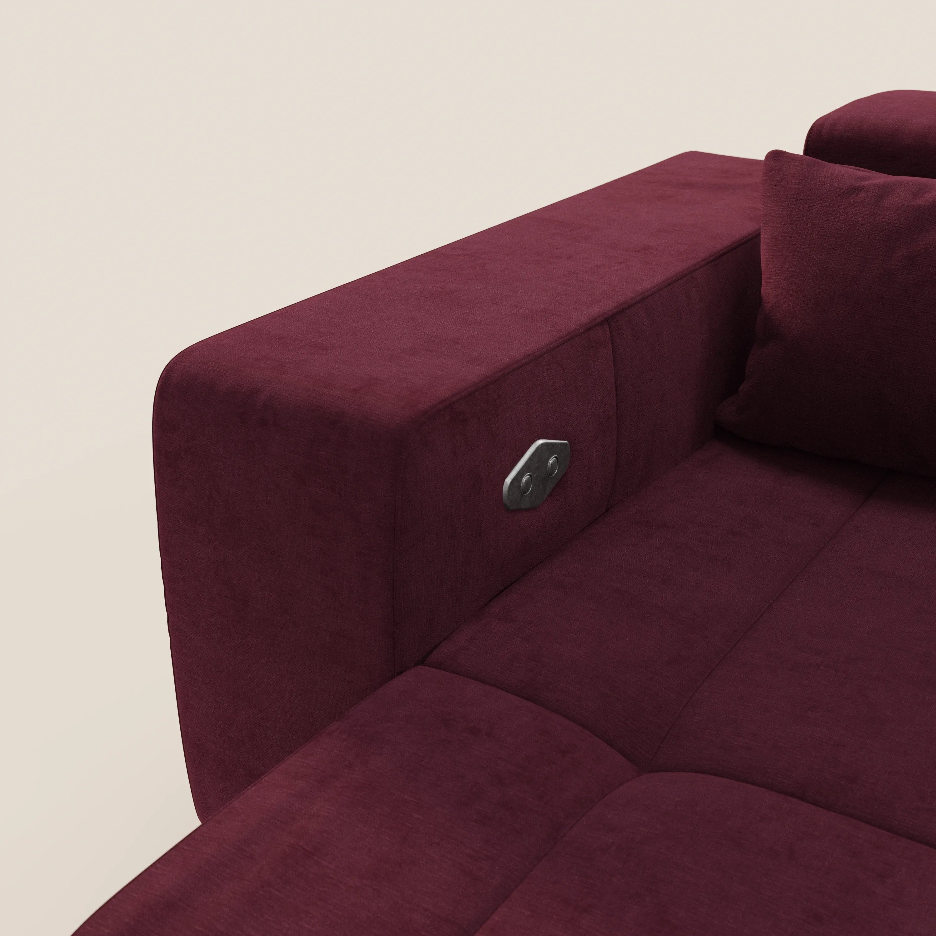 Un primo piano del Divano Monarch con Relax Elettrico T31 di Divani.Store in colore marrone mostra il bracciolo rettangolare con una presa di corrente metallica incorporata (2 porte USB) e un cuscino abbinato. Lo sfondo è un semplice beige chiaro.