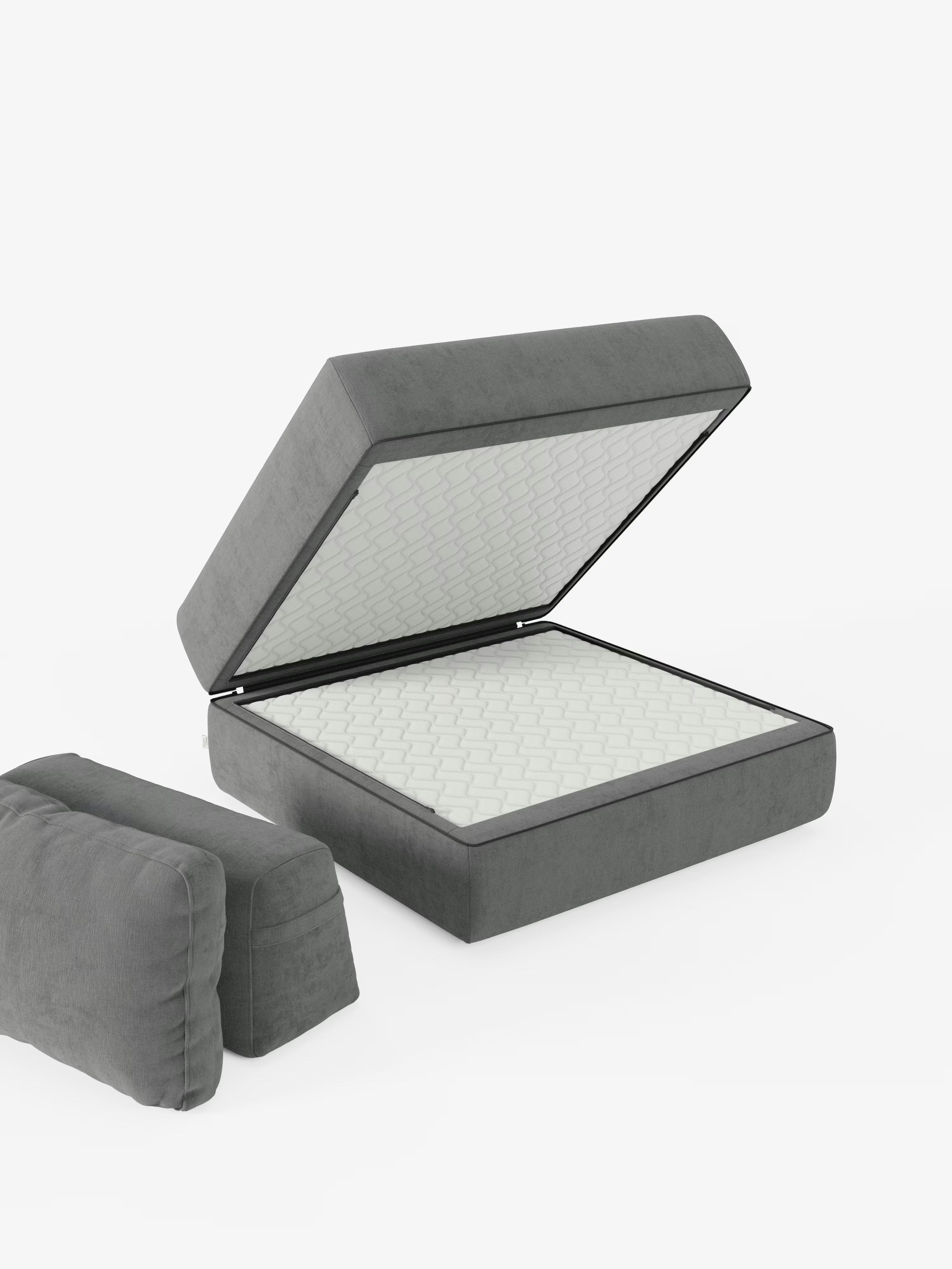 Una “Rift poltrona letto” grigia di Divani.Store, dotata di un materasso in memory foam alto 24 cm e di uno schienale regolabile, è raffigurata con la base imbottita e sollevata, che rivela l’ampio vano contenitore al suo interno. Due cuscini grigi abbinati, ispirati allo stesso design, sono posizionati a terra nelle vicinanze, su uno sfondo bianco a tinta unita.