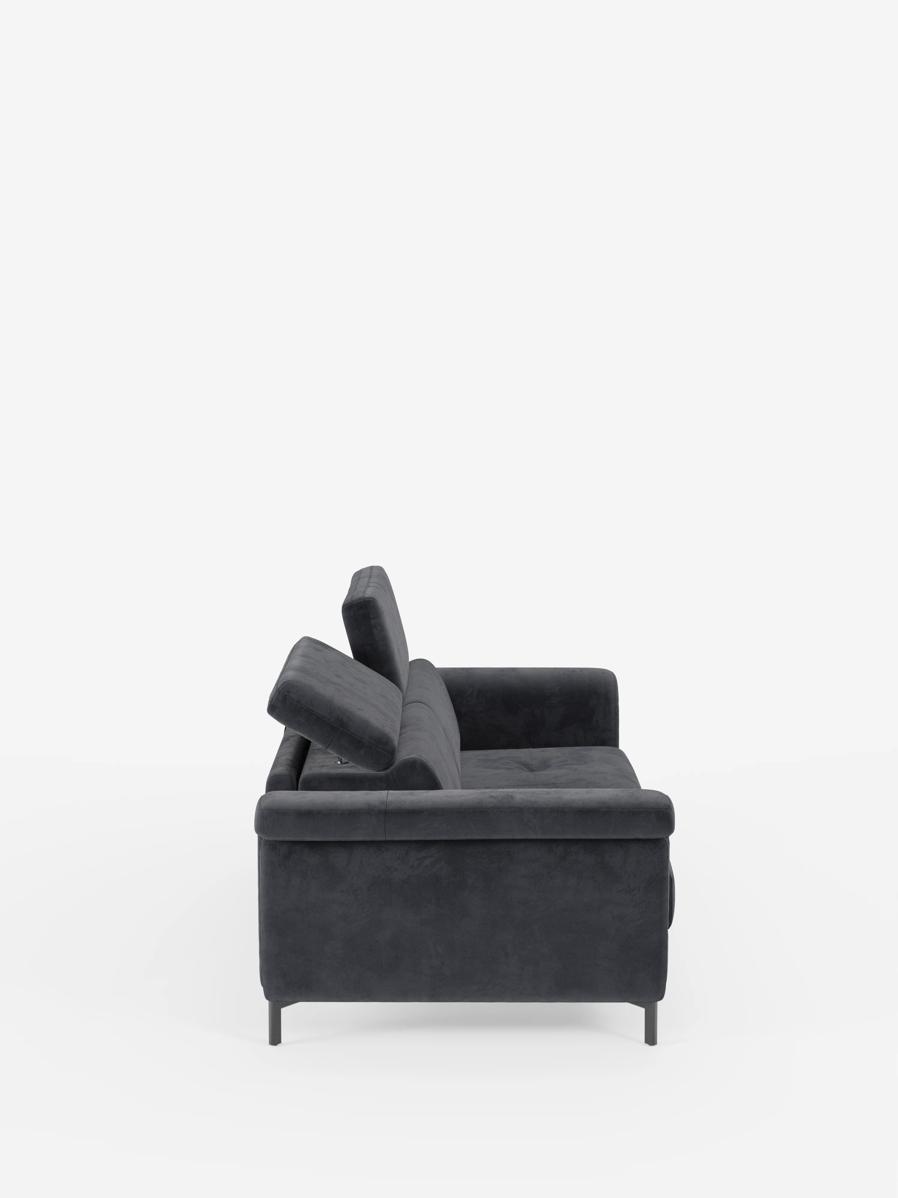 Vista laterale del divano letto di design Capri di Divani.Store, caratterizzato da un tessuto effetto velluto smacchiabile T30 grigio scuro e resistente alle macchie, poggiatesta regolabili, morbidi cuscini e sottili gambe alte nere — esempio di manifattura italiana — su uno sfondo bianco a tinta unita.