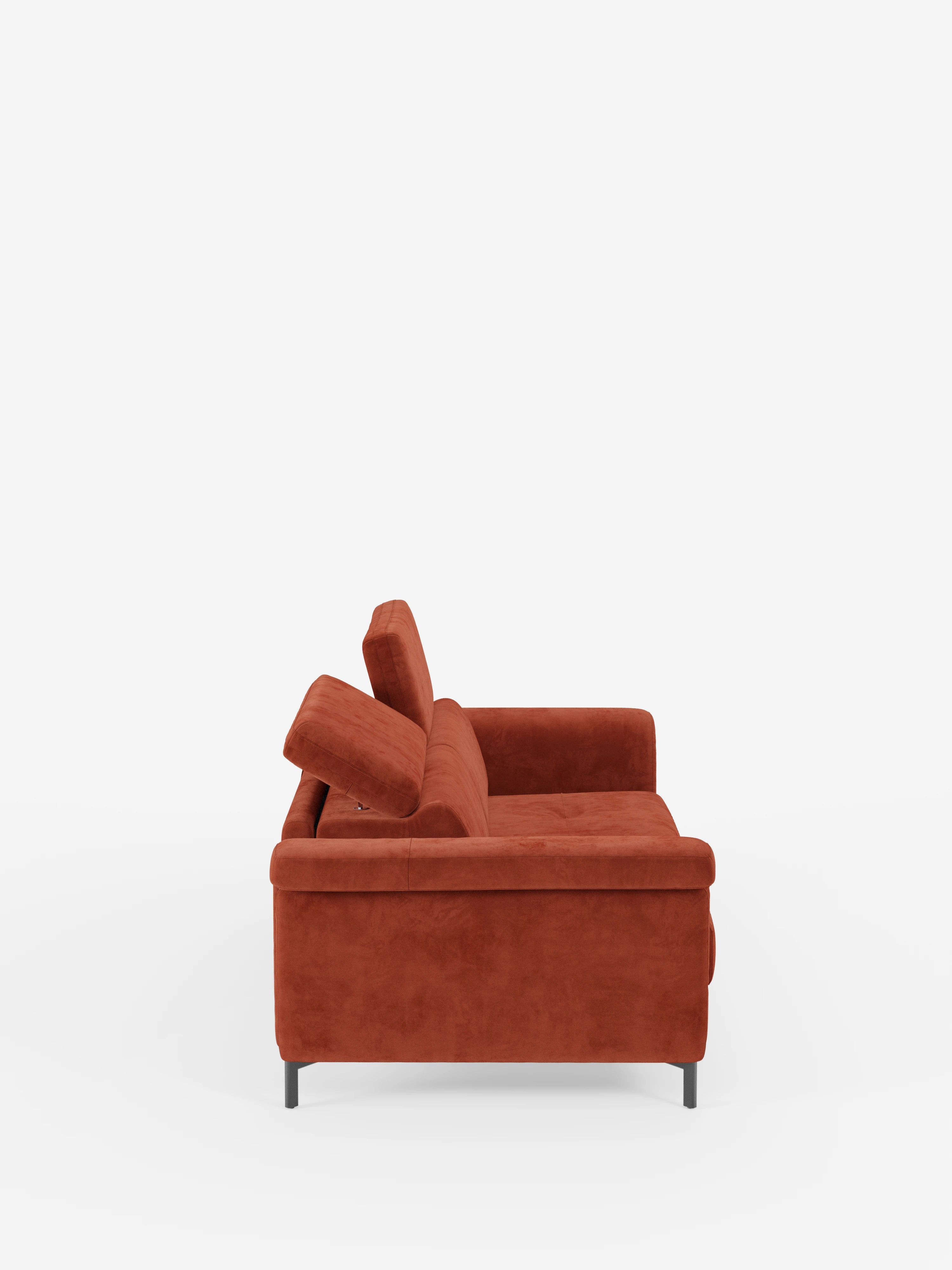 Vista laterale del divano letto di design Capri di Divani.Store, rivestito in raffinato tessuto effetto velluto smacchiabile T30 di colore rosso ruggine, caratterizzato da linee pulite, morbidi cuscini, sottili piedini alti in metallo nero e poggiatesta reclinabili regolabili, il tutto su uno sfondo bianco a tinta unita.