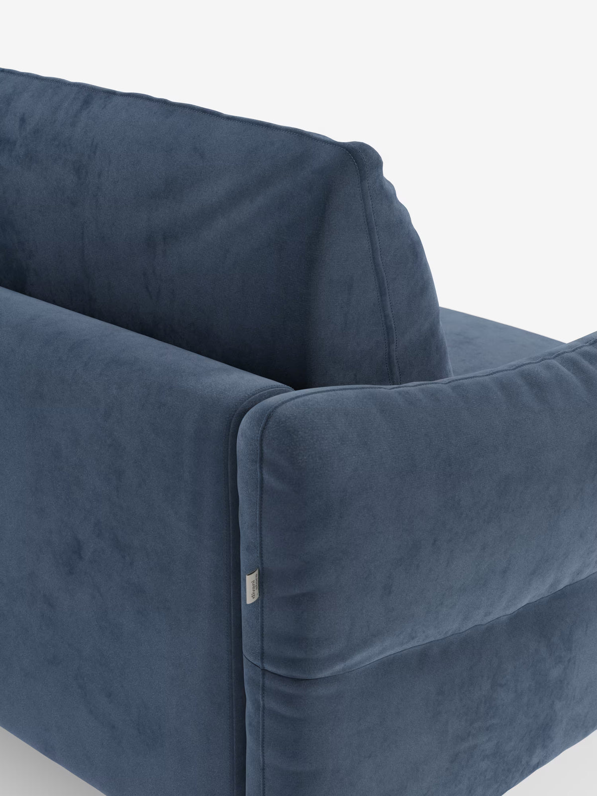 Primo piano del divano letto Dalia di Divani.Store, rivestito in moderno tessuto “vellutino” blu T30 resistente alle macchie. L’immagine mette in risalto la parte superiore dello schienale, i braccioli generosamente imbottiti e le cuciture di precisione. Si nota la trama morbida e liscia, insieme a una piccola etichetta in tessuto cucita nella cucitura. Lo sfondo è bianco a tinta unita.