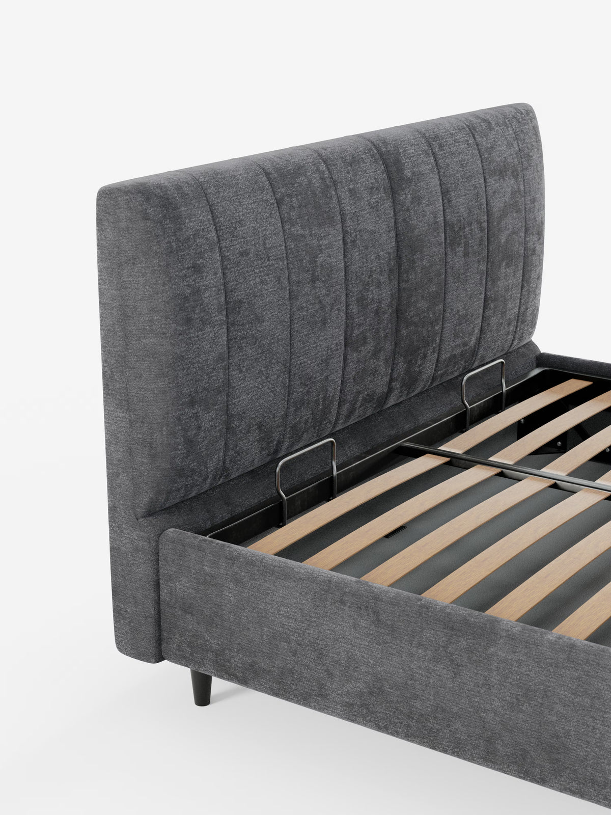 Un primo piano del letto imbottito ONYX con contenitore e testiera verticale in tessuto certificato Oeko-Tex® di Letti.store, caratterizzato da una testiera alta, imbottita, di colore grigio scuro e con cuciture verticali. La struttura comprende doghe in legno e barre di sostegno in metallo nero, completate da gambe corte nere. Lo sfondo è bianco a tinta unita.