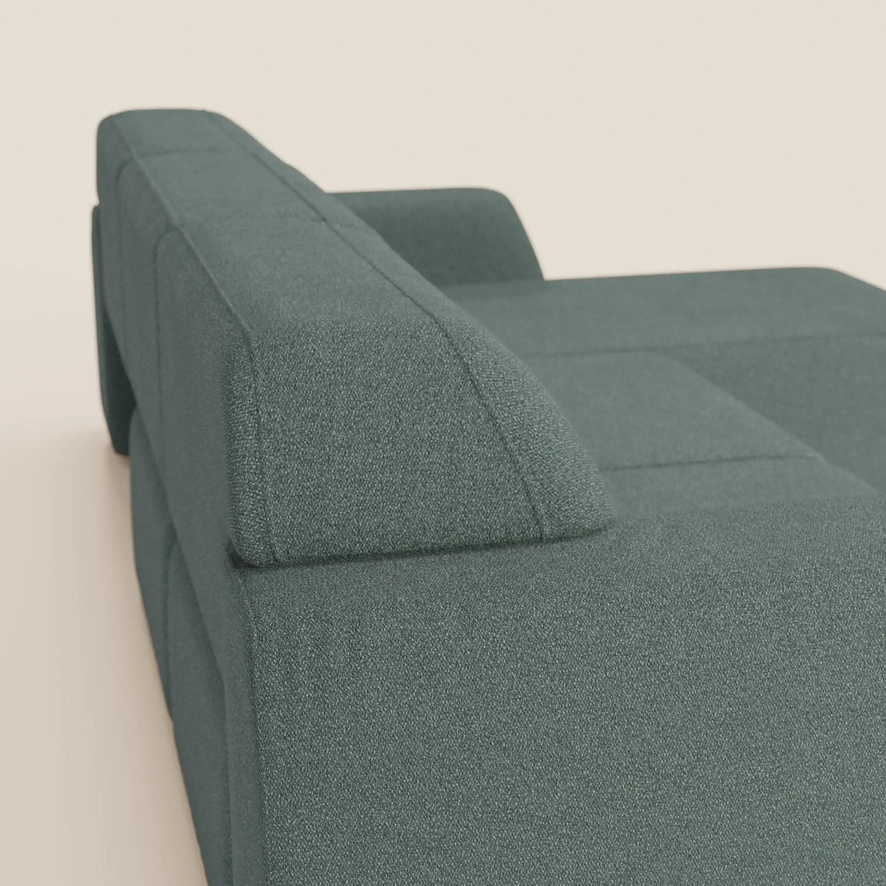 Una vista angolata e ravvicinata del divano angolare Divani.Store Orbit con penisola reversibile e sedute allungabili in tessuto smacchiabile effetto cotone T33, che mostra parte dello schienale verde moderno, della seduta e del bracciolo squadrato su uno sfondo bianco sporco.