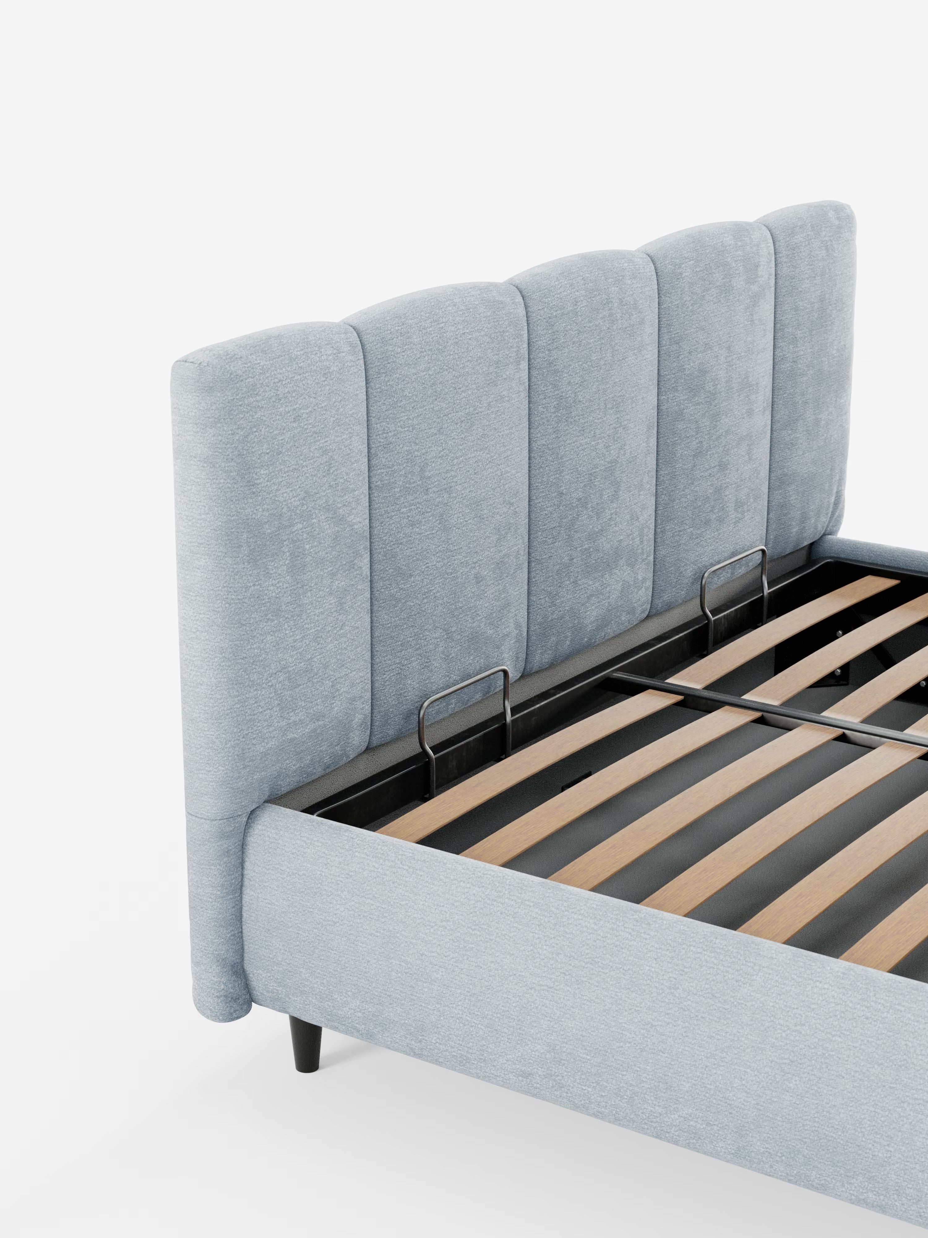 Un primo piano del letto imbottito ARKAM con contenitore e testiera a lavorazione verticale di Letti.store mette in risalto il rivestimento grigio chiaro certificato Oeko-Tex® e la testiera alta, curva e con pannelli verticali. Il pratico design in stile shabby chic mette in evidenza le robuste doghe in legno e la struttura in metallo nero all’interno della base contenitore. Il letto, con le sue corte gambe nere, spicca con eleganza su uno sfondo bianco.