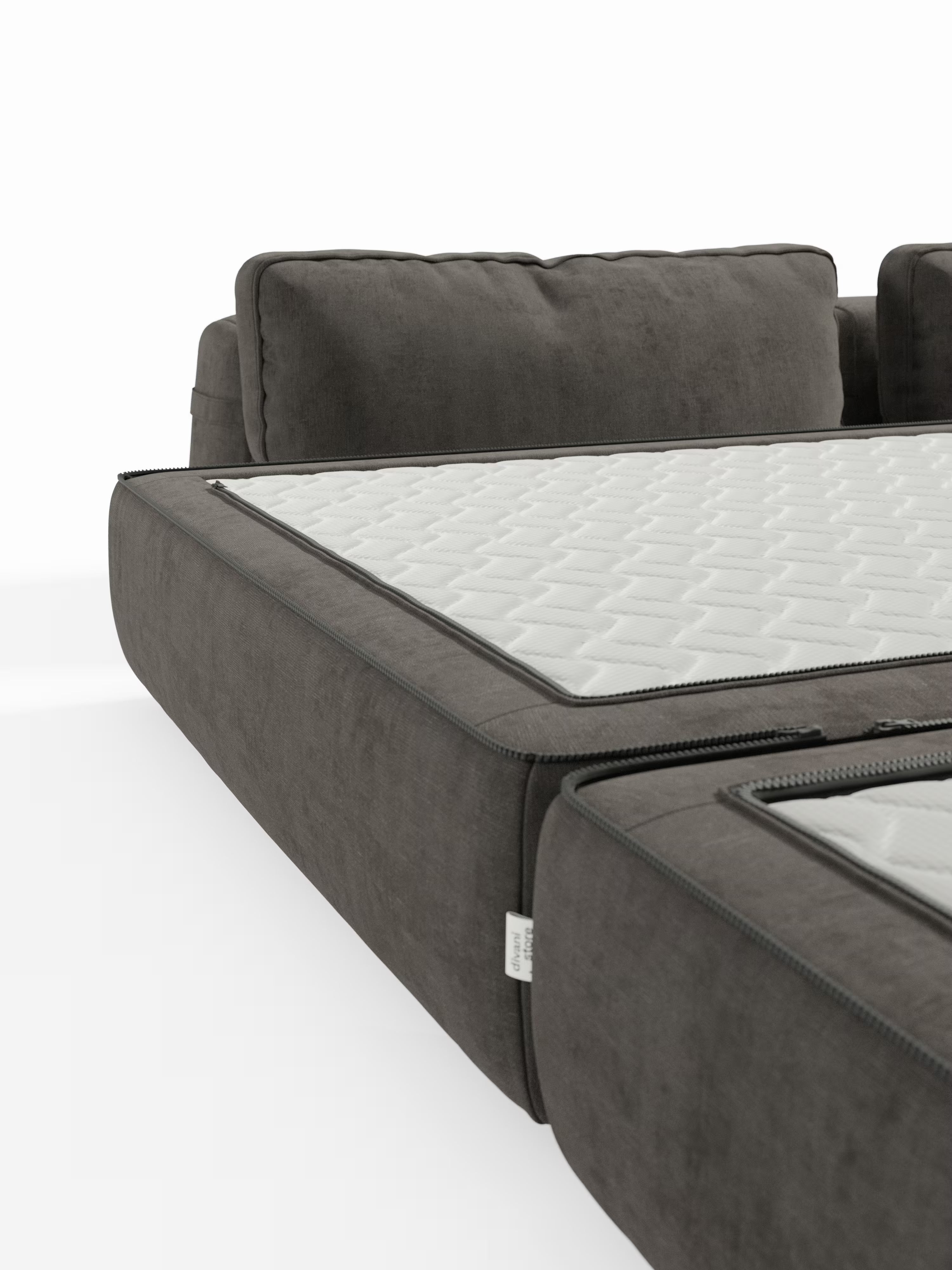 Un primo piano del divano letto matrimoniale Rift, disponibile nelle versioni a 2 e 3 posti, di colore grigio scuro, realizzato da Divani.Store, caratterizzato da schienali regolabili e da un materasso in memory foam T31 dello spessore di 22 cm. Al sedile è fissato un coprimaterasso bianco trapuntato con chiusura a zip e motivo geometrico, che ricorda i materassi in memory foam di alta qualità. Lo sfondo è bianco a tinta unita, con solo una parte dello schienale e del sedile del divano in primo piano.