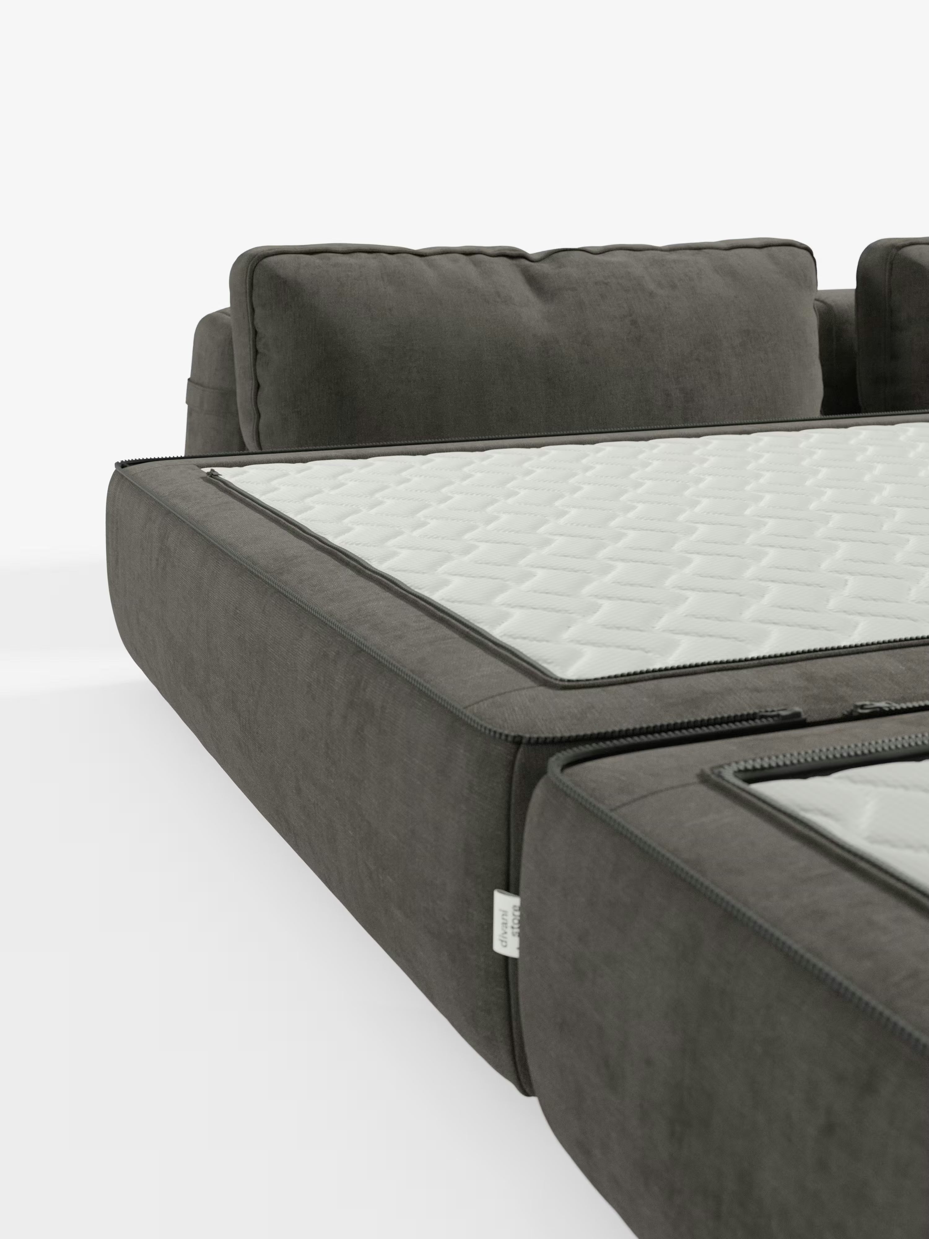 Un primo piano del divano letto matrimoniale Rift a 2 e 3 posti con schienali mobili di Divani.Store, in grigio scuro, mette in risalto il suo design moderno grazie al coprimaterasso bianco trapuntato con cerniera, ben visibile sulla seduta. Questo divano letto è dotato di morbidi cuscini dello schienale e include un materasso in memory foam alto 24 cm rivestito in tessuto T31 facile da pulire, il tutto su uno sfondo bianco a tinta unita.