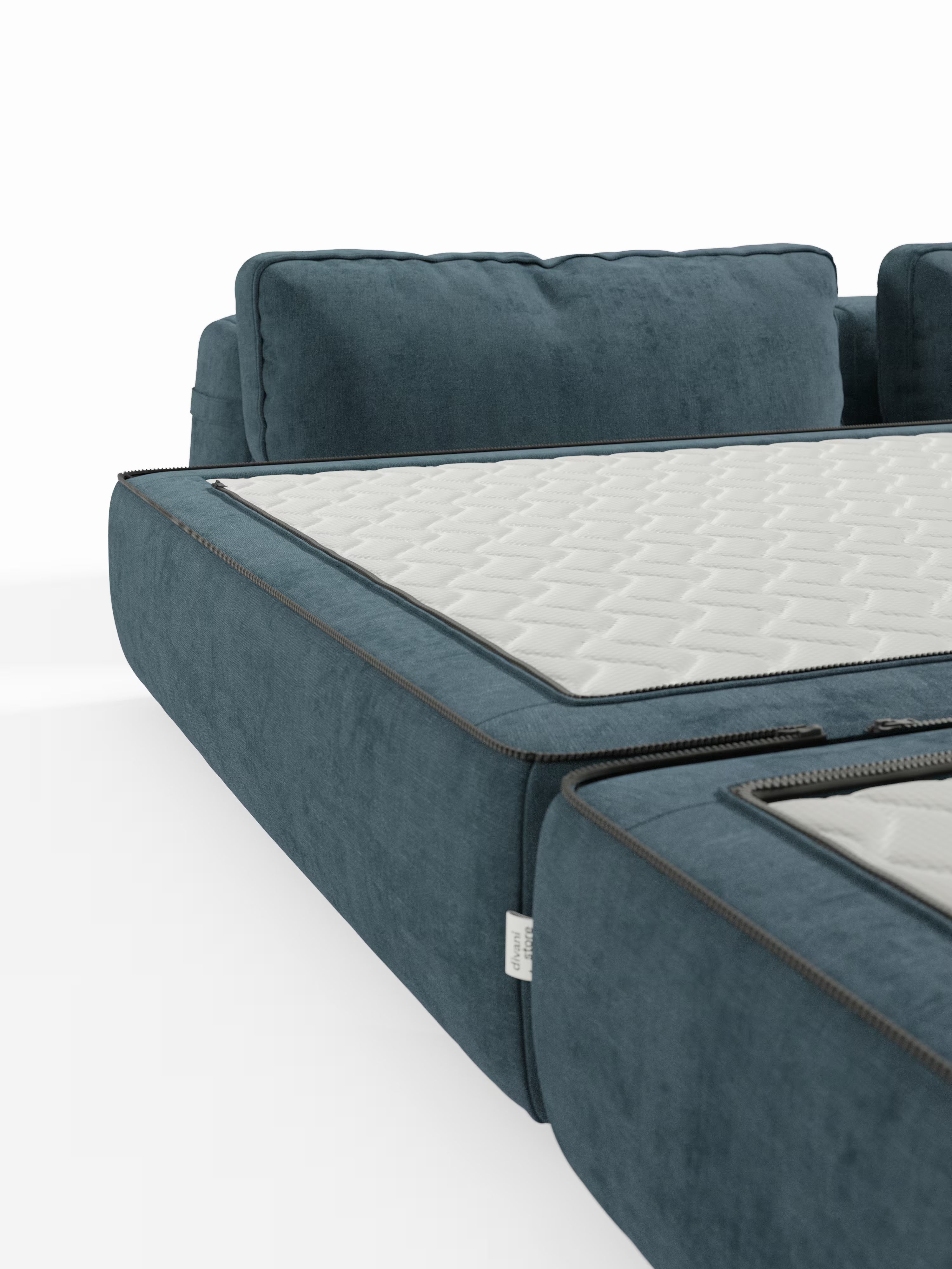Un primo piano del divano letto matrimoniale Rift a 2 e 3 posti con schienali mobili di Divani.Store, un moderno divano imbottito blu dotato di un materasso alto 22 cm con schiuma memory T31. Il coprimaterasso bianco è aperto con la cerniera e parzialmente visibile sulla seduta, mettendo in risalto la sua trama trapuntata e i dettagli della cerniera su uno sfondo bianco a tinta unita, per un comfort ancora maggiore.
