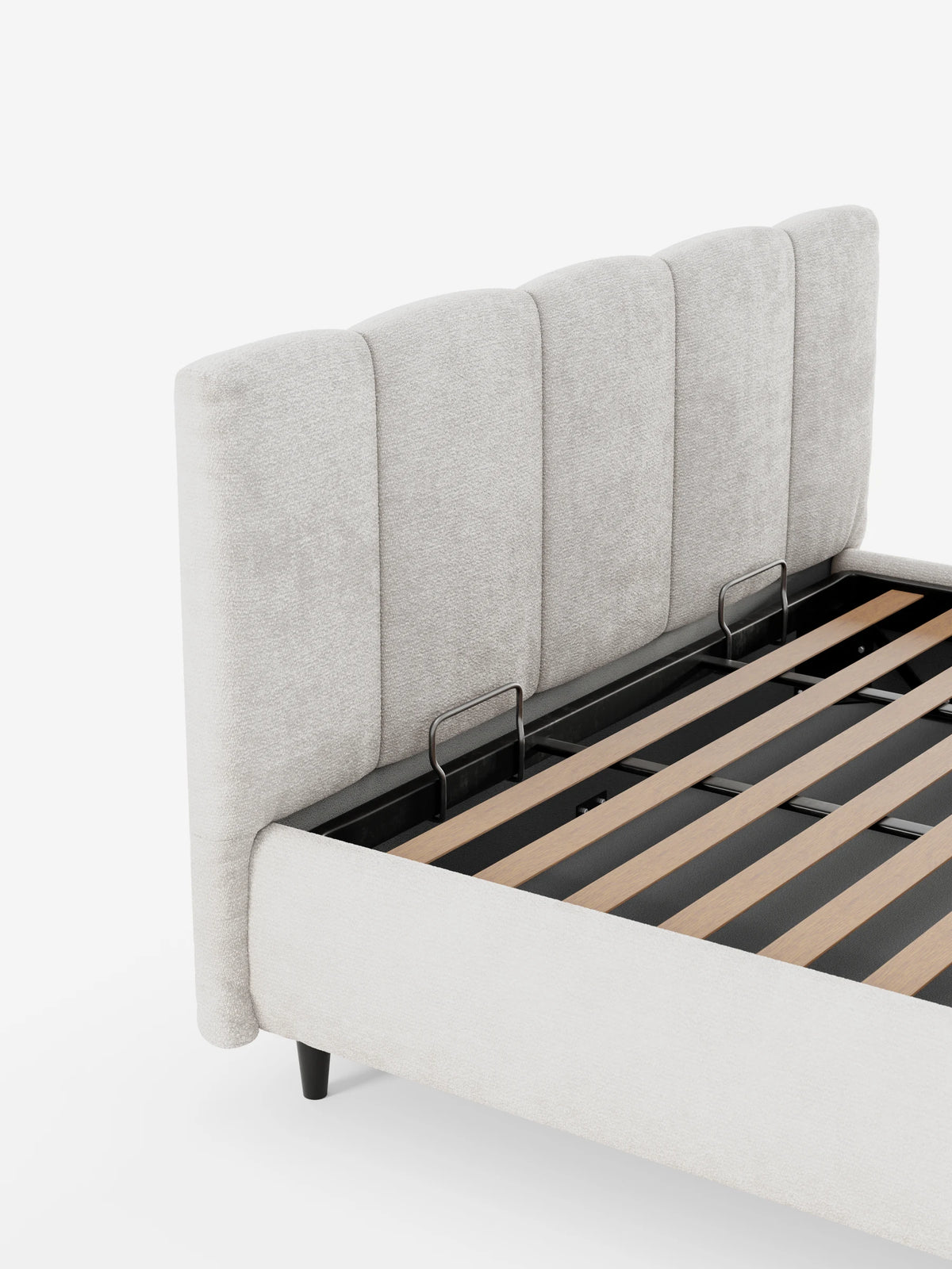 Il letto imbottito ARKAM con contenitore e testiera a lavorazione verticale è un letto in tessuto beige chiaro, caratterizzato da un'alta testiera trapuntata verticalmente, una base aperta con doghe in legno e un meccanismo di contenimento in metallo su sfondo bianco.