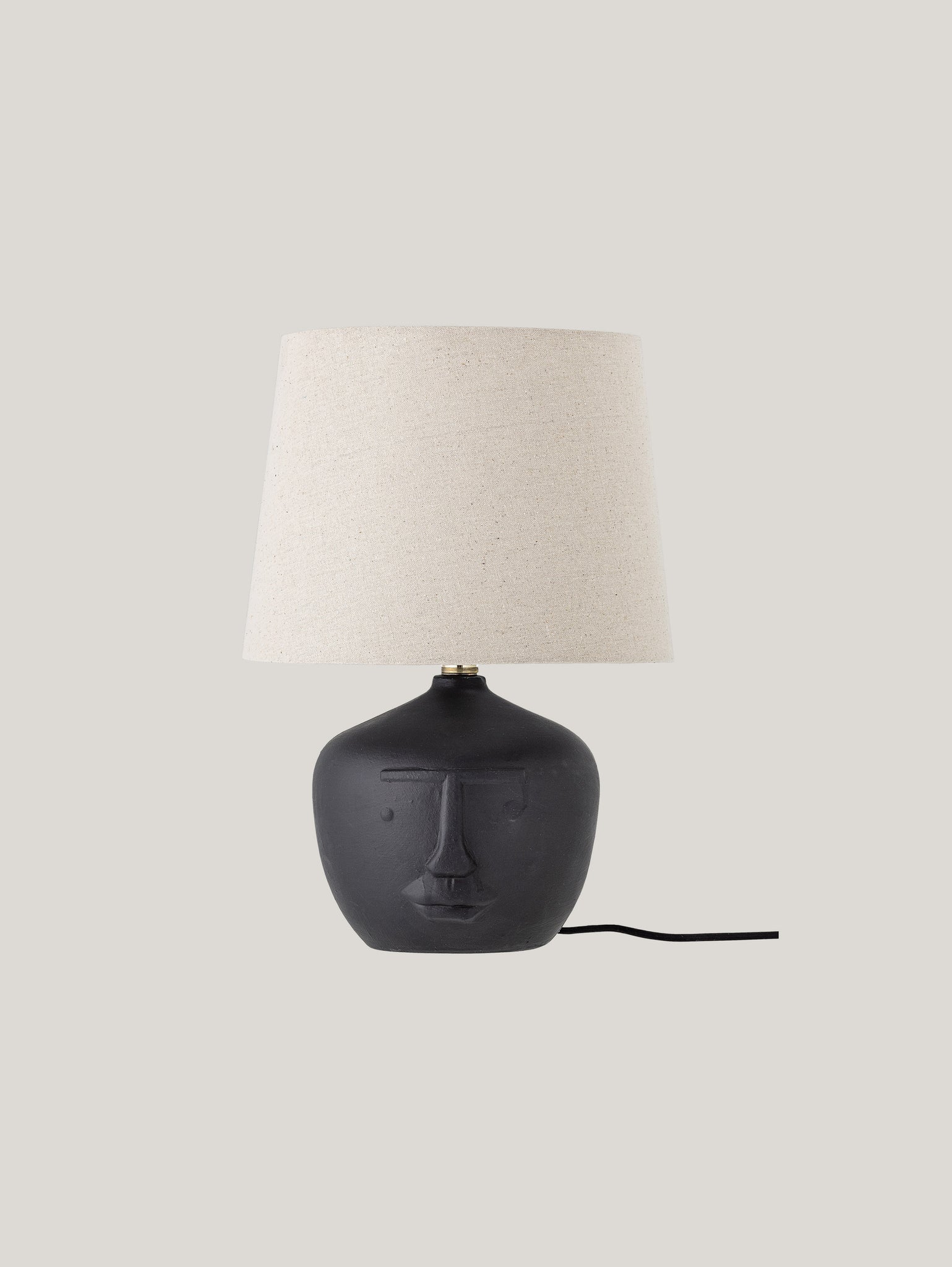 La Matheo Lampada da Tavolo di Divani.Store presenta una base in terracotta con finitura nera opaca, progettata con elementi facciali stilizzati che intrecciano Design e Arte. Sormontata da un Paralume beige in Lino, si erge elegantemente su uno sfondo grigio chiaro, evidenziato dal suo caratteristico cordone nero visibile.