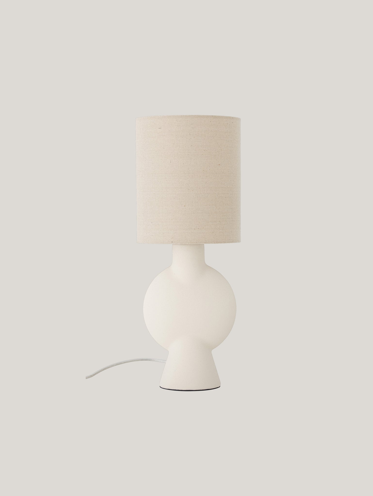 La lampada da tavolo Sergio di Divani.Store sfoggia un design minimalista, con una base sferica bianca realizzata in gres Stoneware e un paralume cilindrico beige in lino. Il suo cavo elettrico bianco si estende sottilmente dalla base, il tutto su uno sfondo grigio chiaro.