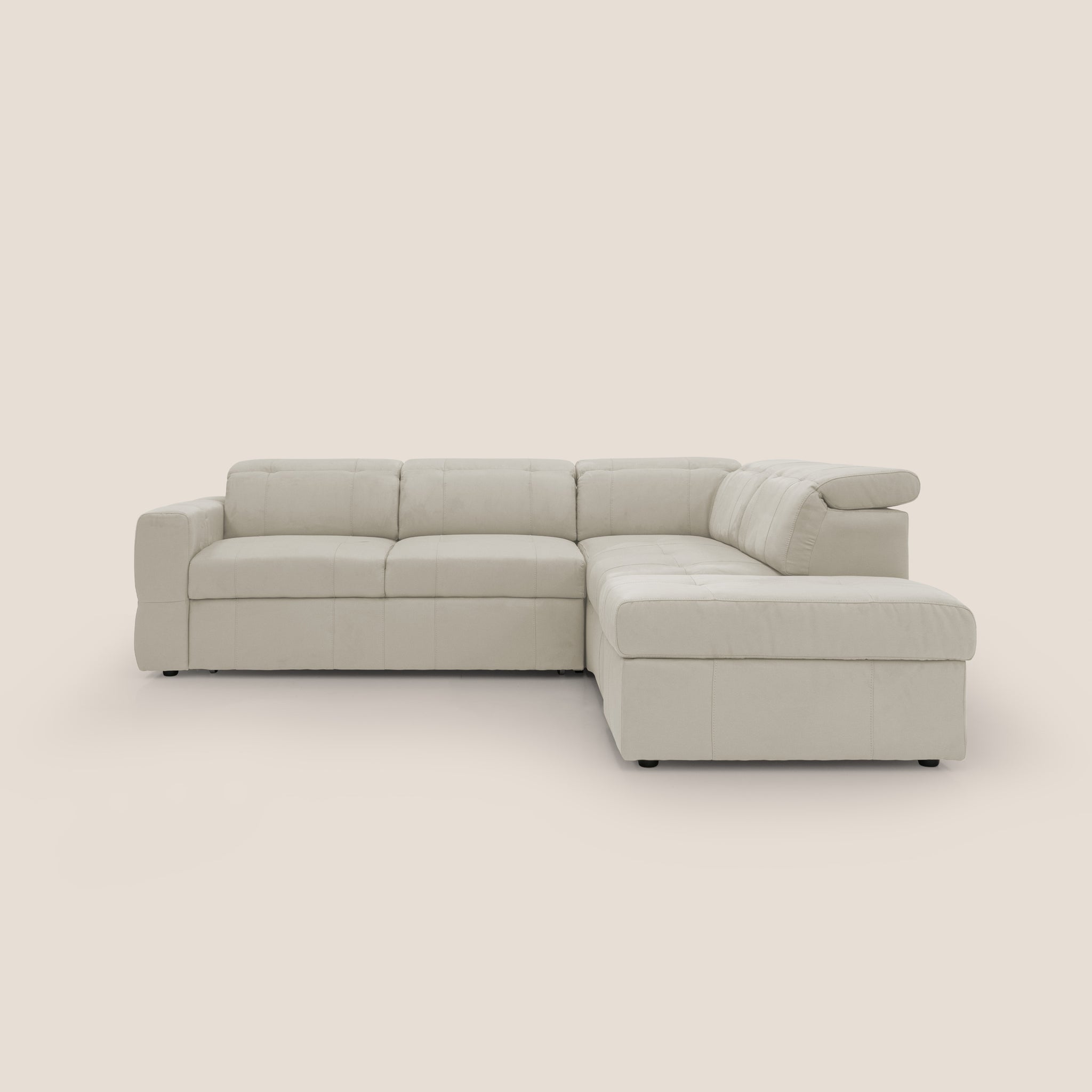 Un divano componibile beige Kronos a L di Divani.Store è posizionato su uno sfondo chiaro e semplice. Questo divano angolare in microfibra impermeabile T11 presenta cuscini trapuntati, una chaise longue sul lato destro, sedute ampie e braccioli bassi, incarnando un design moderno con un fascino elegante e minimalista. Inoltre, include un poggiapiedi estraibile e un pouf contenitore mobile per una maggiore funzionalità.