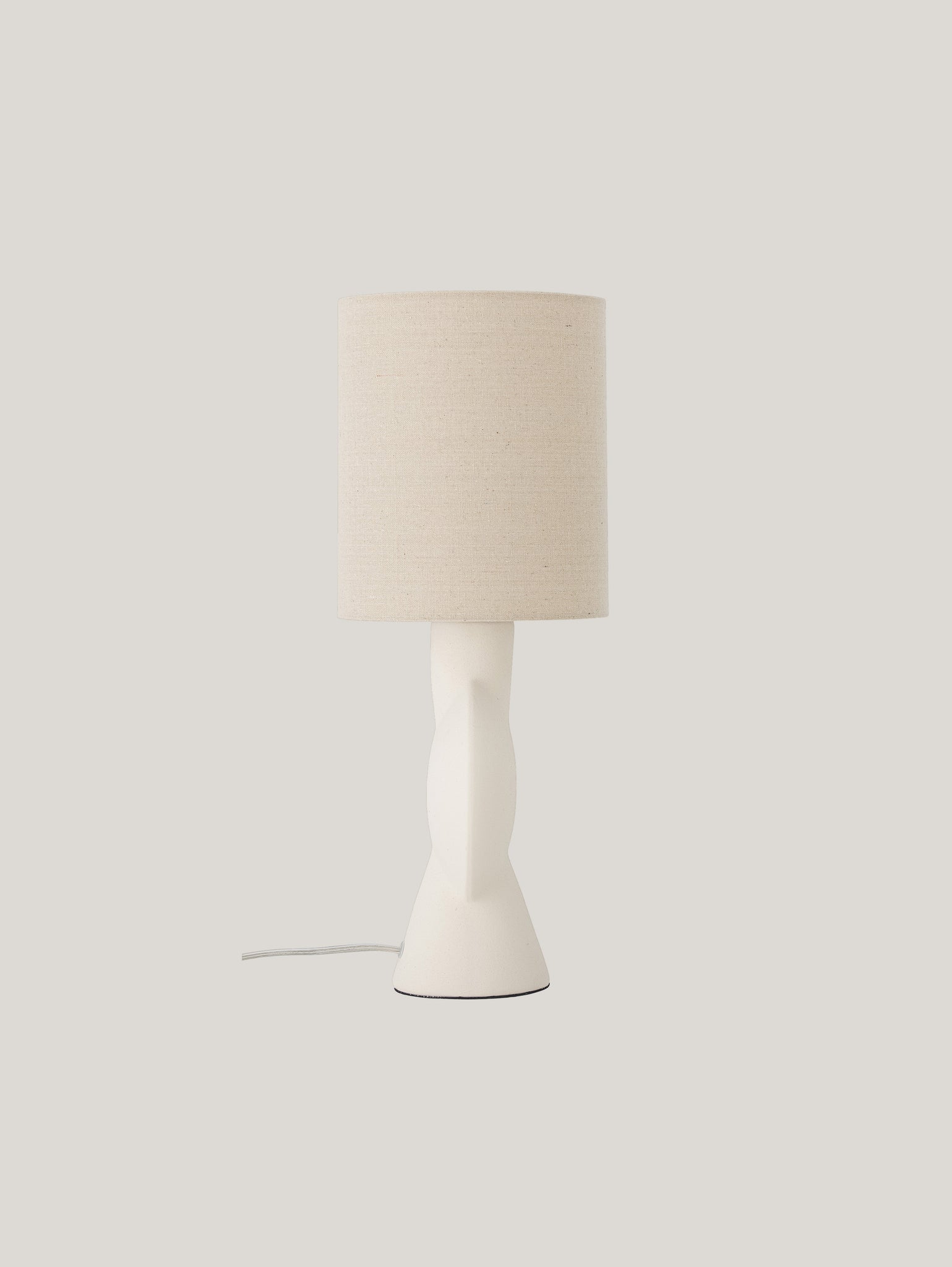 La lampada da tavolo Sergio di Divani.Store è caratterizzata da una base intrecciata in ceramica gres bianco opaco ed è completata da un paralume cilindrico in lino beige. Il cavo parzialmente visibile si estende dalla base, mentre lo sfondo grigio chiaro semplice accentua il design minimalista di questa moderna lampada da tavolo.