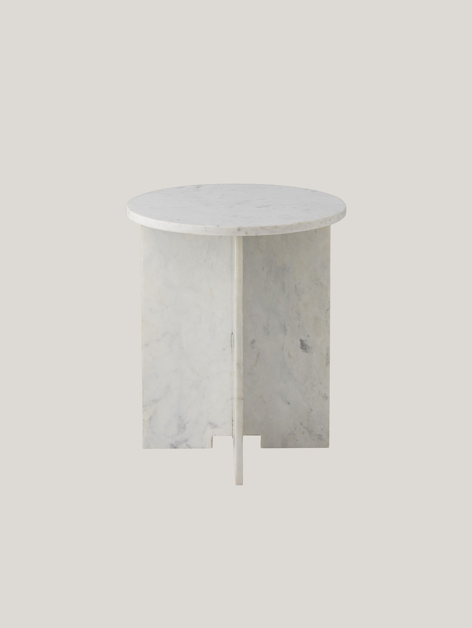 Ecco Jasmia tavolino tondo in marmo bianco di Divani.Store, un tavolino rotondo minimalista con una superficie liscia in marmo bianco. La sua base è formata da quattro pannelli piatti intersecati, elegantemente adagiati su uno sfondo grigio chiaro. Le sottili venature grigie del marmo aggiungono consistenza e raffinatezza al suo design moderno.