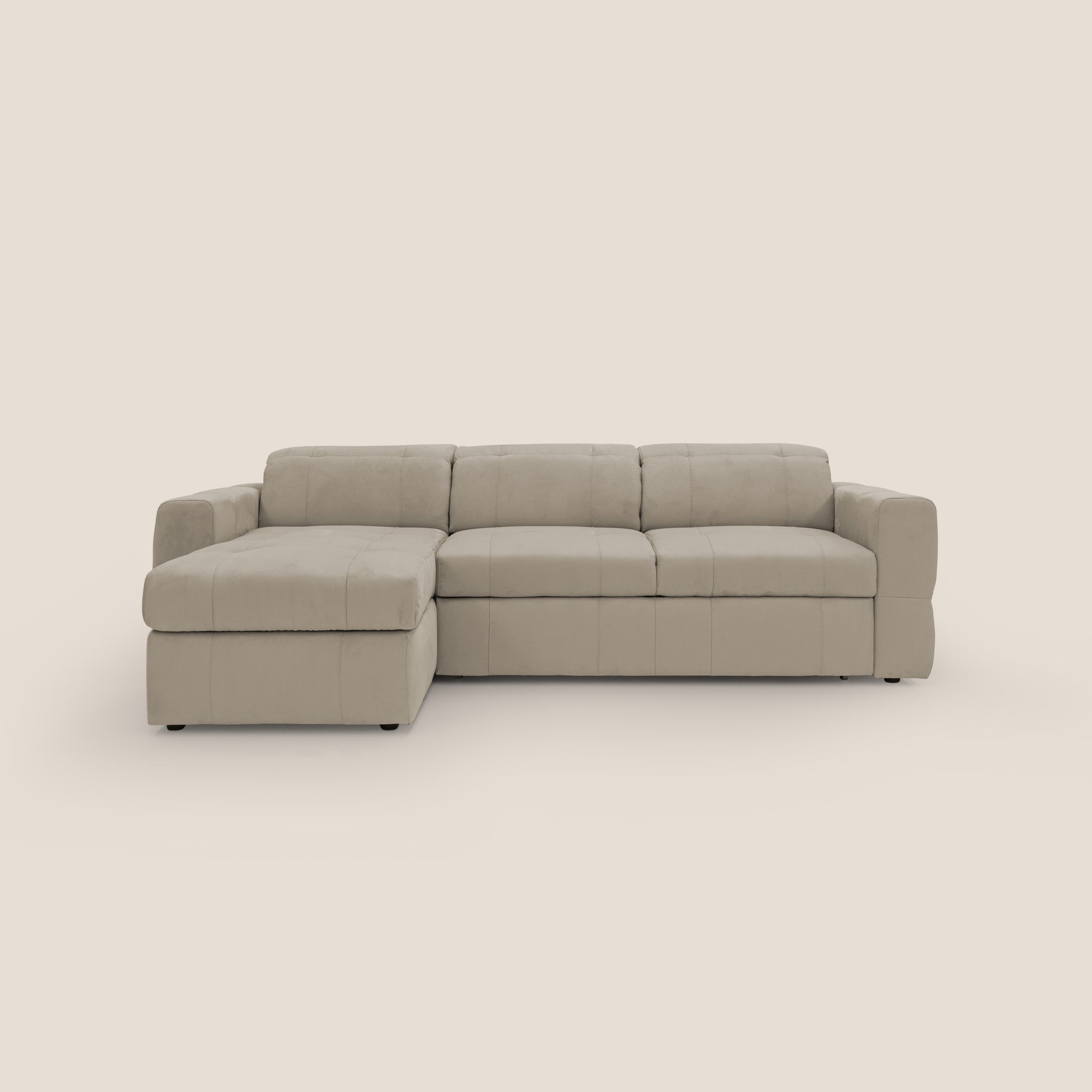 Un Divano angolare beige Kronos di Divani.Store, con cuscini morbidi e trapuntati, è posizionato su uno sfondo neutro. Realizzato in Italia, include una chaise longue sul lato sinistro per una seduta spaziosa. Il rivestimento morbido in microfibra e il design moderno minimalista offrono un'estetica moderna e confortevole.