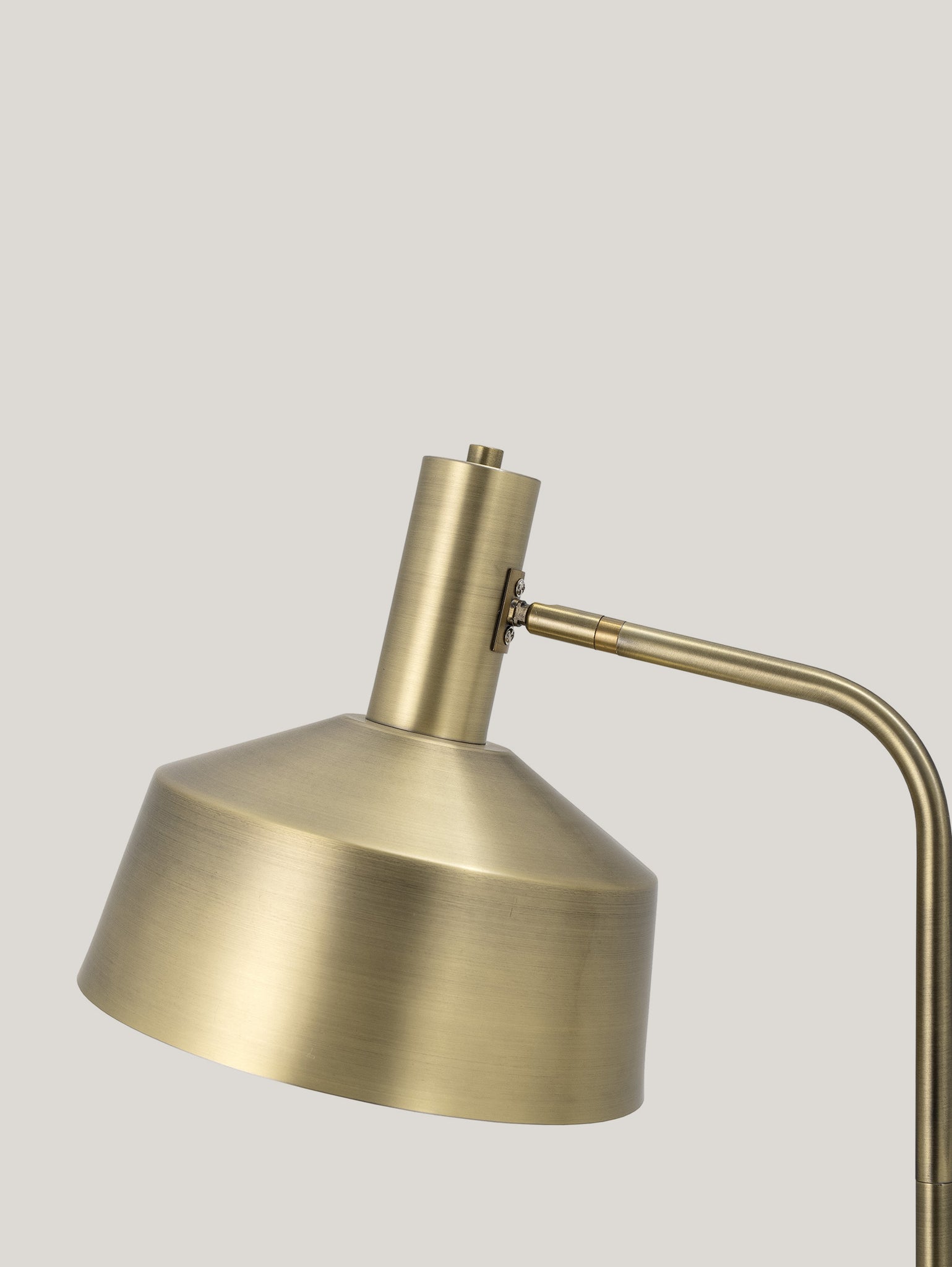 Primo piano della lampada da terra Lissa in metallo colore ottone di Divani.Store su uno sfondo grigio chiaro. Questa lampada da tavolo in ottone presenta un collo cilindrico e un paralume angolato e largo, che trasuda eleganza classica con il suo design elegante e minimalista e la finitura in metallo spazzolato che incarna il design sofisticato.