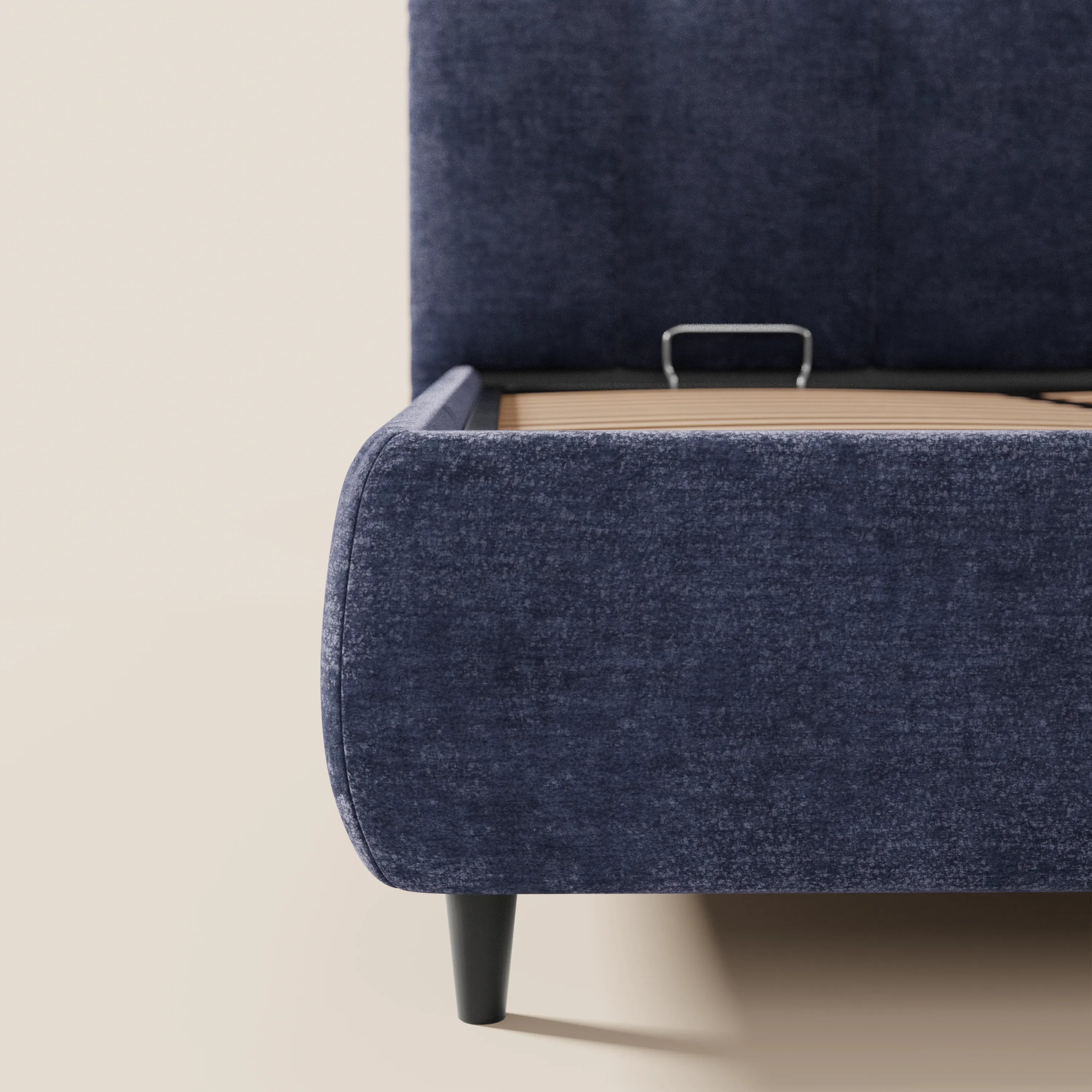 Un primo piano del letto imbottito ARKAM con contenitore di Letti.store, realizzato in tessuto Oeko-Tex® blu scuro, caratterizzato da una testiera con lavorazione verticale, angoli arrotondati e gambe angolate nere, su uno sfondo beige chiaro.