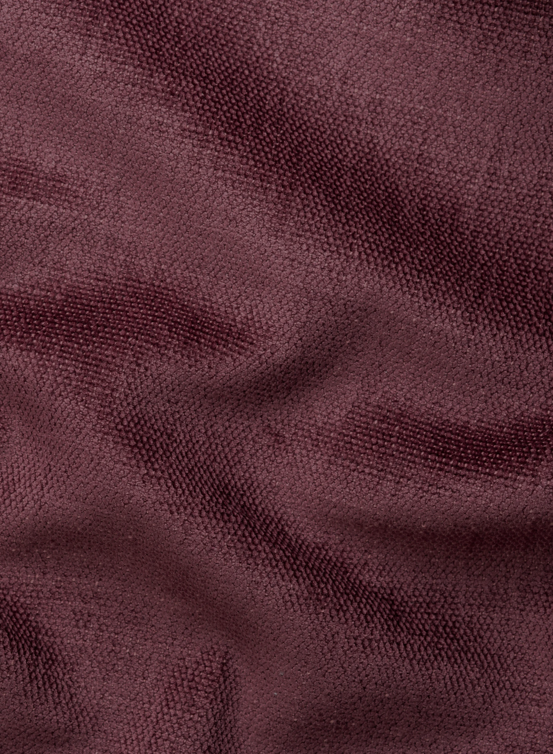 Un primo piano del tessuto color bordeaux intenso che riveste un divano letto angolare Ischia con schienali traslanti, che mostra una trama ben definita con morbide pieghe arricciate che creano un gioco sottile di luci e ombre sulla superficie.
