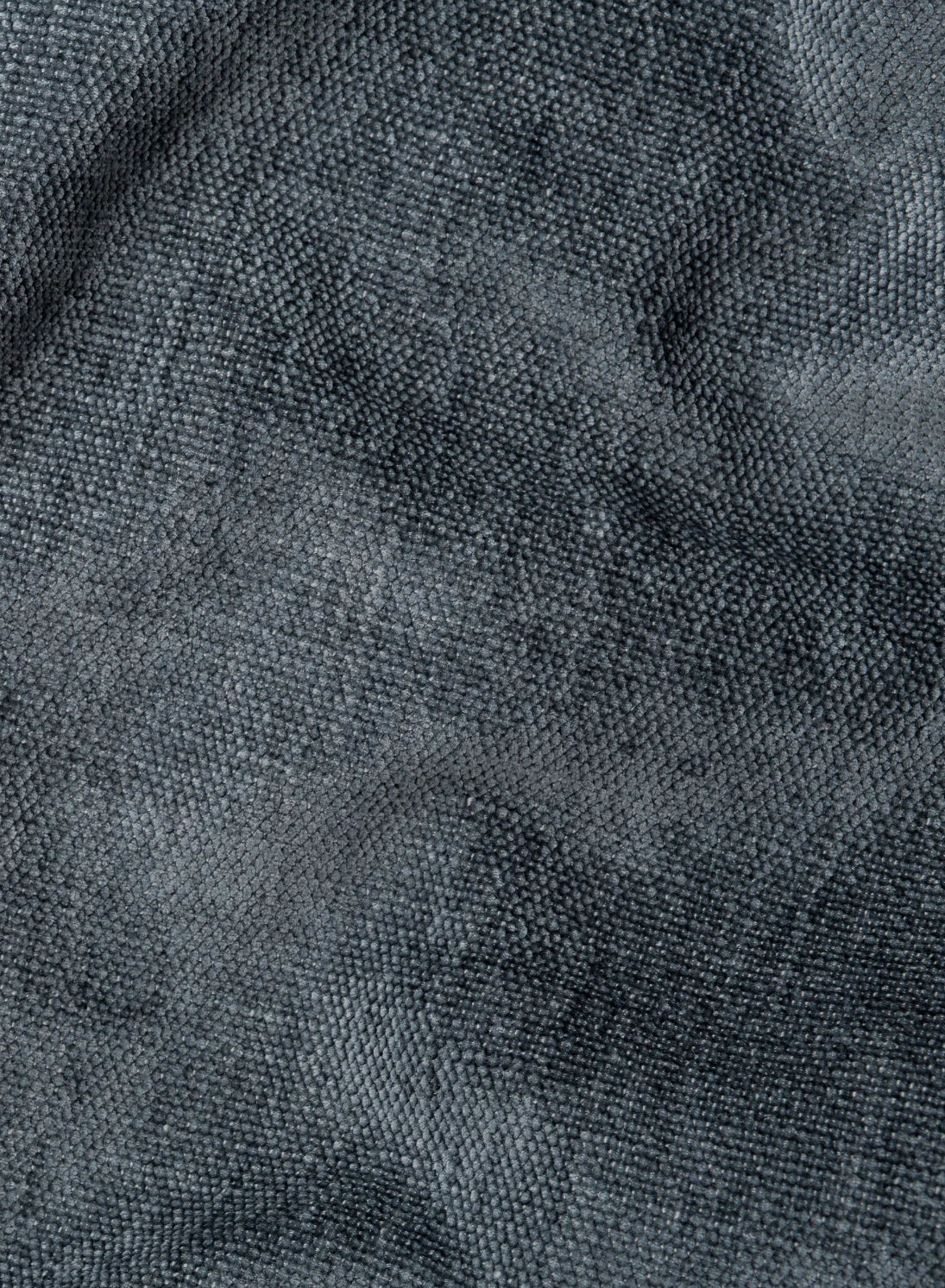 Primo piano sul tessuto grigio scuro a trama grossolana di un divano a 3 posti di Ischia con pouf estraibile e schienali traslanti in tessuto misto lino lavabile, che mostra morbide pieghe ricche di texture con sottili giochi di luce e ombra.