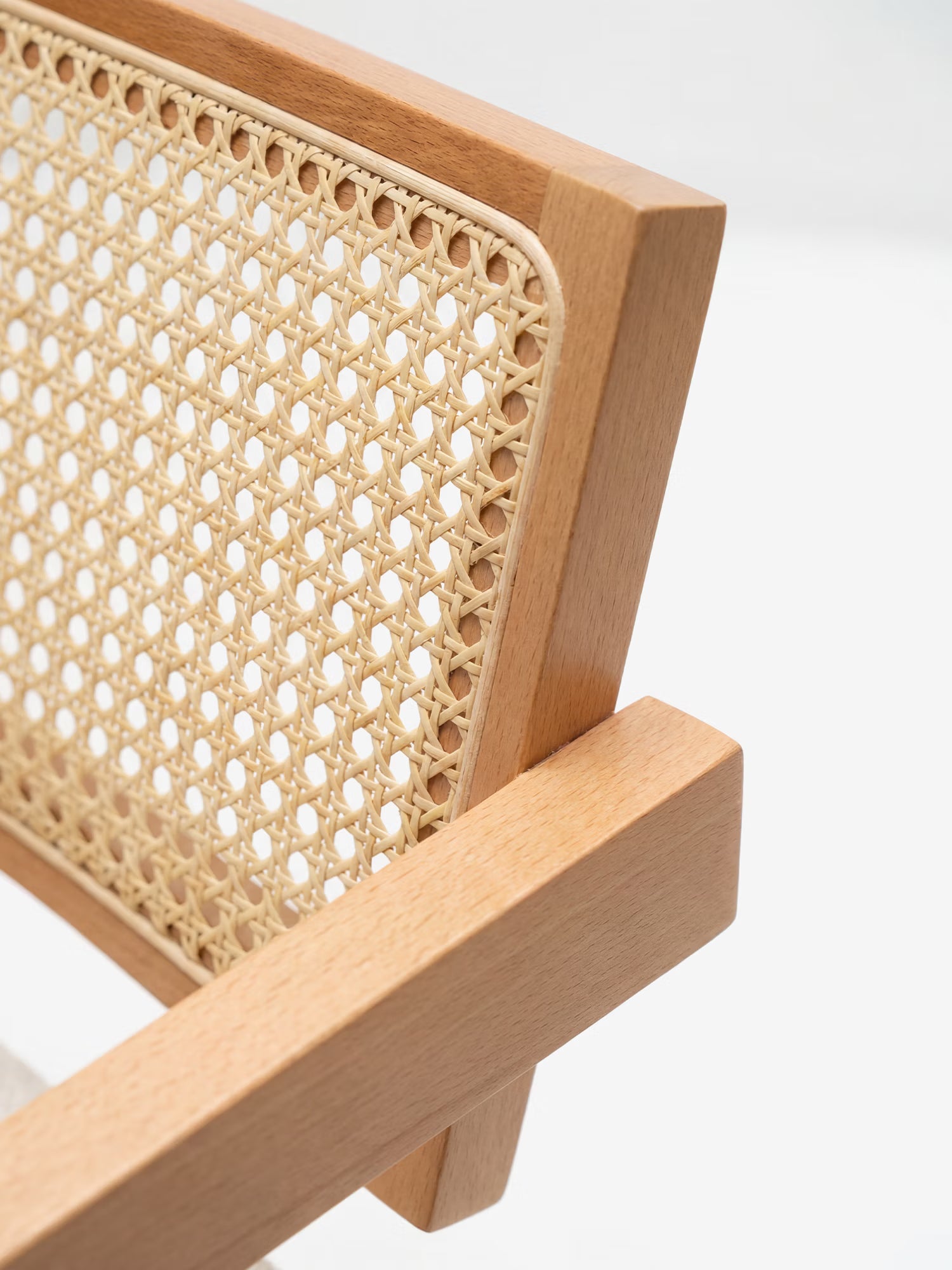 Primo piano della sedia Antea con braccioli in rovere di Divani.Store, con schienale in rattan e seduta imbottita in misto cotone. La struttura angolare in legno chiaro risalta sullo sfondo bianco, mettendo in risalto il suo intricato motivo intrecciato in rattan.