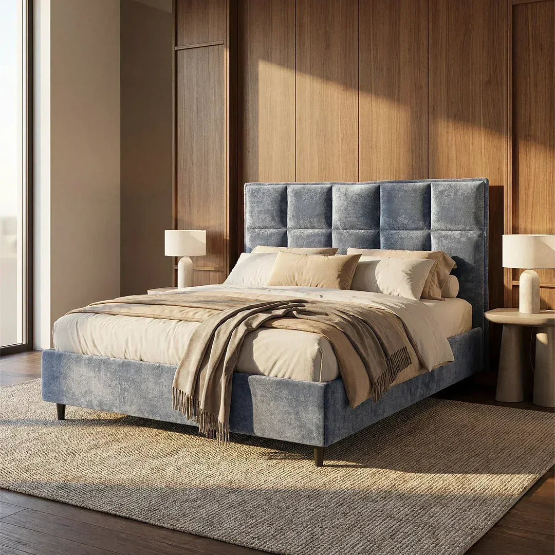 Una camera da letto moderna mette in risalto il letto imbottito AURO con vano contenitore e testiera capitonné alta in ciniglia Oeko-Tex® di Letti.store, nei toni del blu-grigio, con copriletti beige, pareti rivestite in pannelli di legno e lampade bianche, per un look accogliente e luminoso.