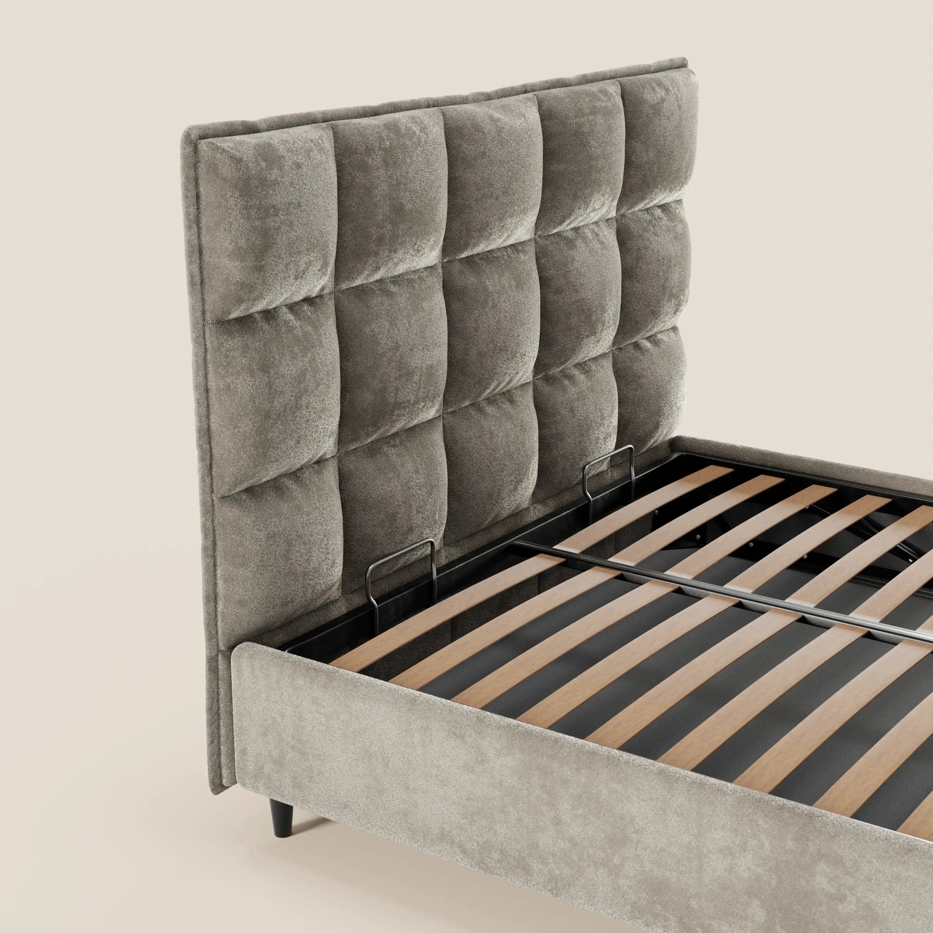 Il letto imbottito AURO di Letti.store presenta una testiera alta e capitonné in ciniglia grigia certificata Oeko-Tex®, doghe in legno e un vano contenitore. Questo elegante letto moderno risalta sullo sfondo beige chiaro.