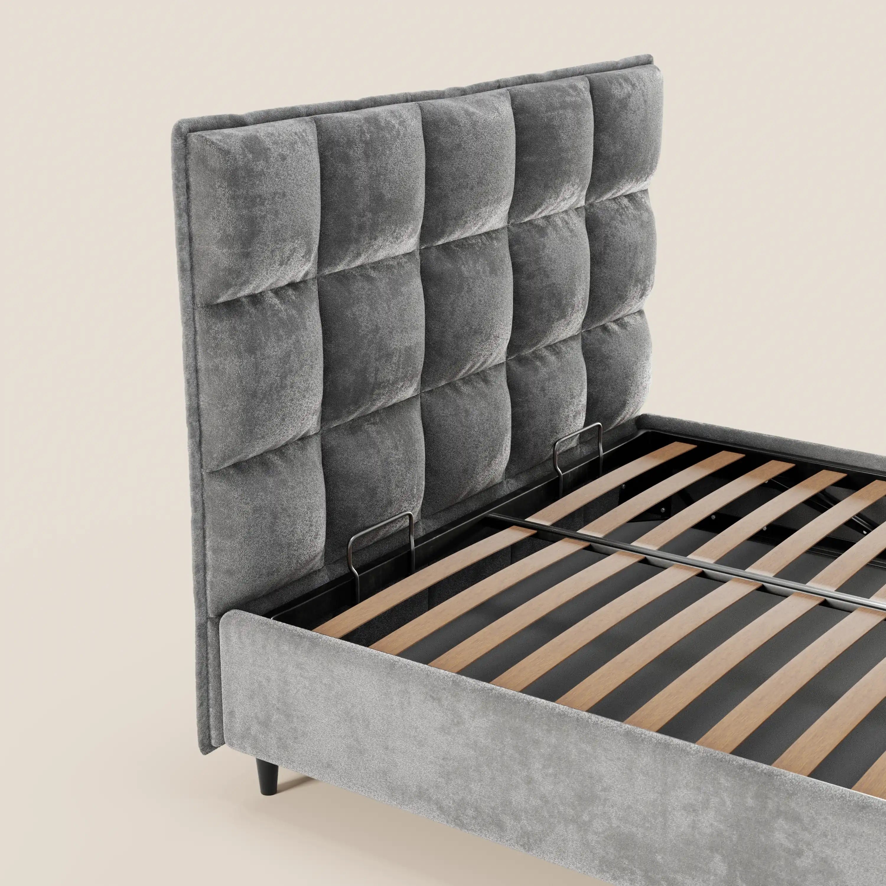 Il letto imbottito AURO di Letti.store presenta una testiera alta e morbida, rifinita con cuciture capitonné in ciniglia grigia certificata Oeko-Tex®, con profili coordinati e doghe a vista in legno chiaro, raffigurato senza materasso su uno sfondo bianco sporco.
