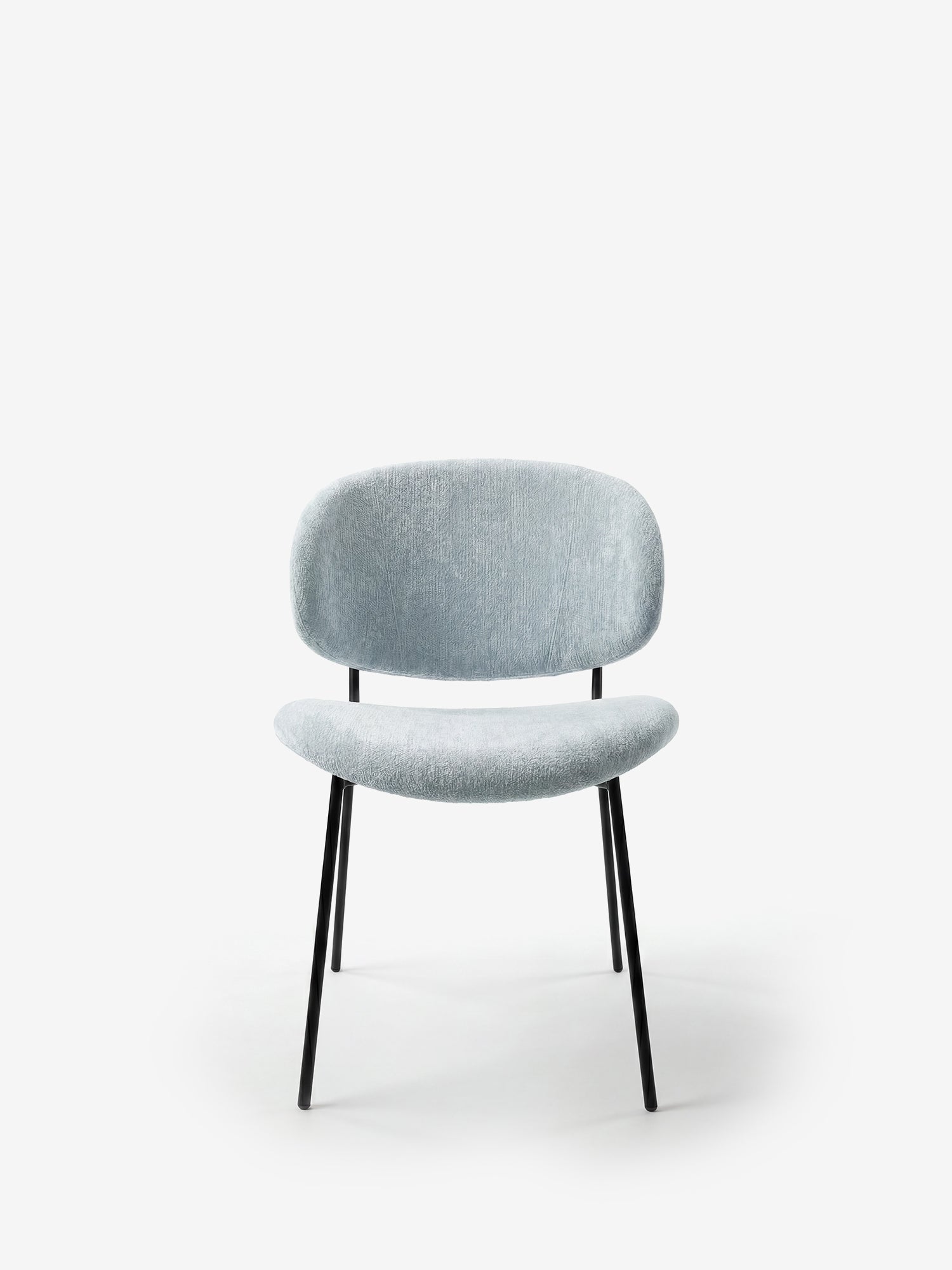 La sedia Bruma di Divani.Store presenta un elegante rivestimento in tessuto goffrato azzurro, uno schienale avvolgente e un design minimalista con sottili gambe angolate in metallo nero, per un tocco contemporaneo su uno sfondo bianco.