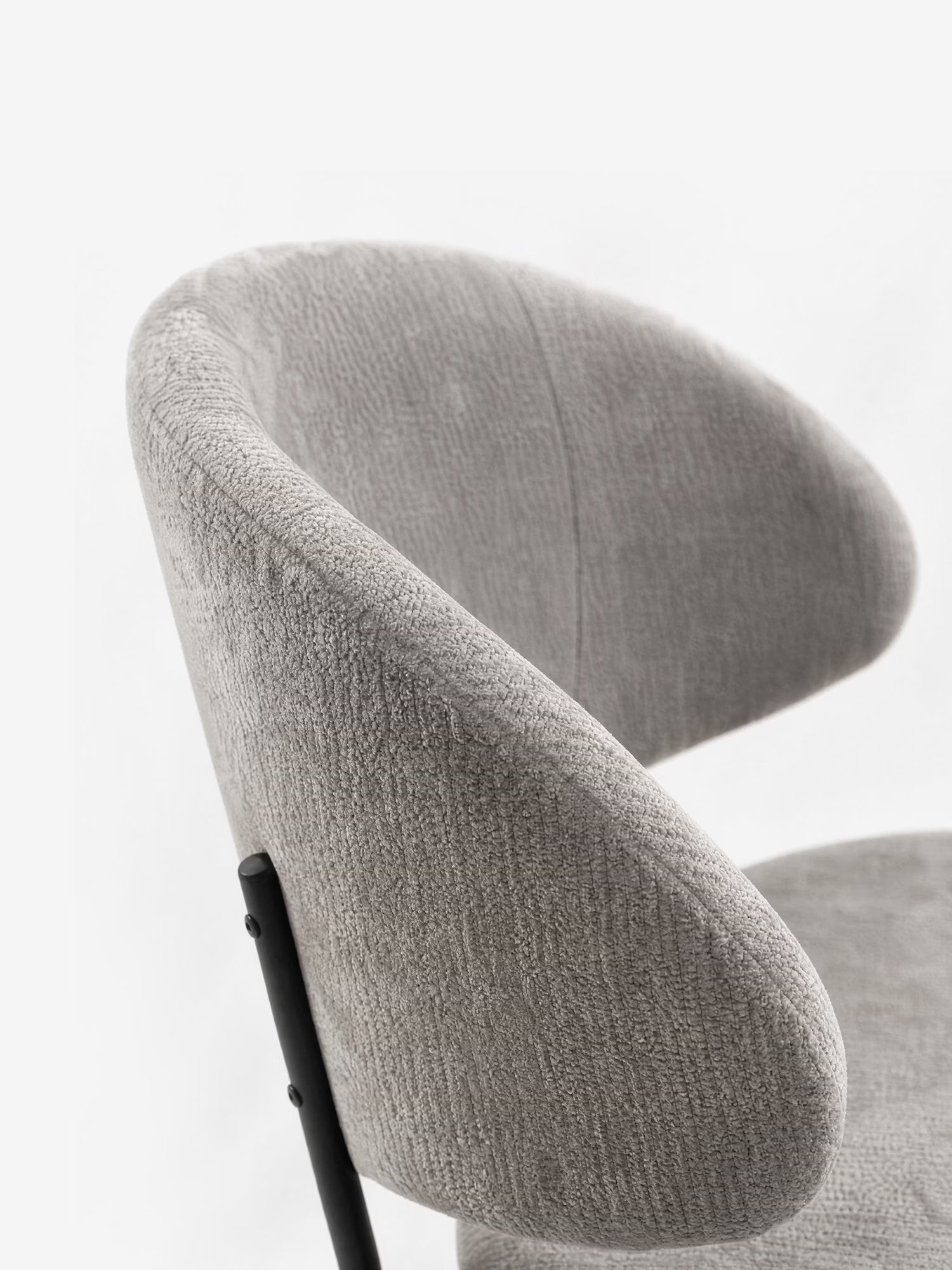 Un primo piano di Bruma di Divani.Store: sedia realizzata in elegante tessuto goffrato grigio chiaro, dal design minimalista con gambe in metallo nero e schienale avvolgente, raffigurata su sfondo bianco.