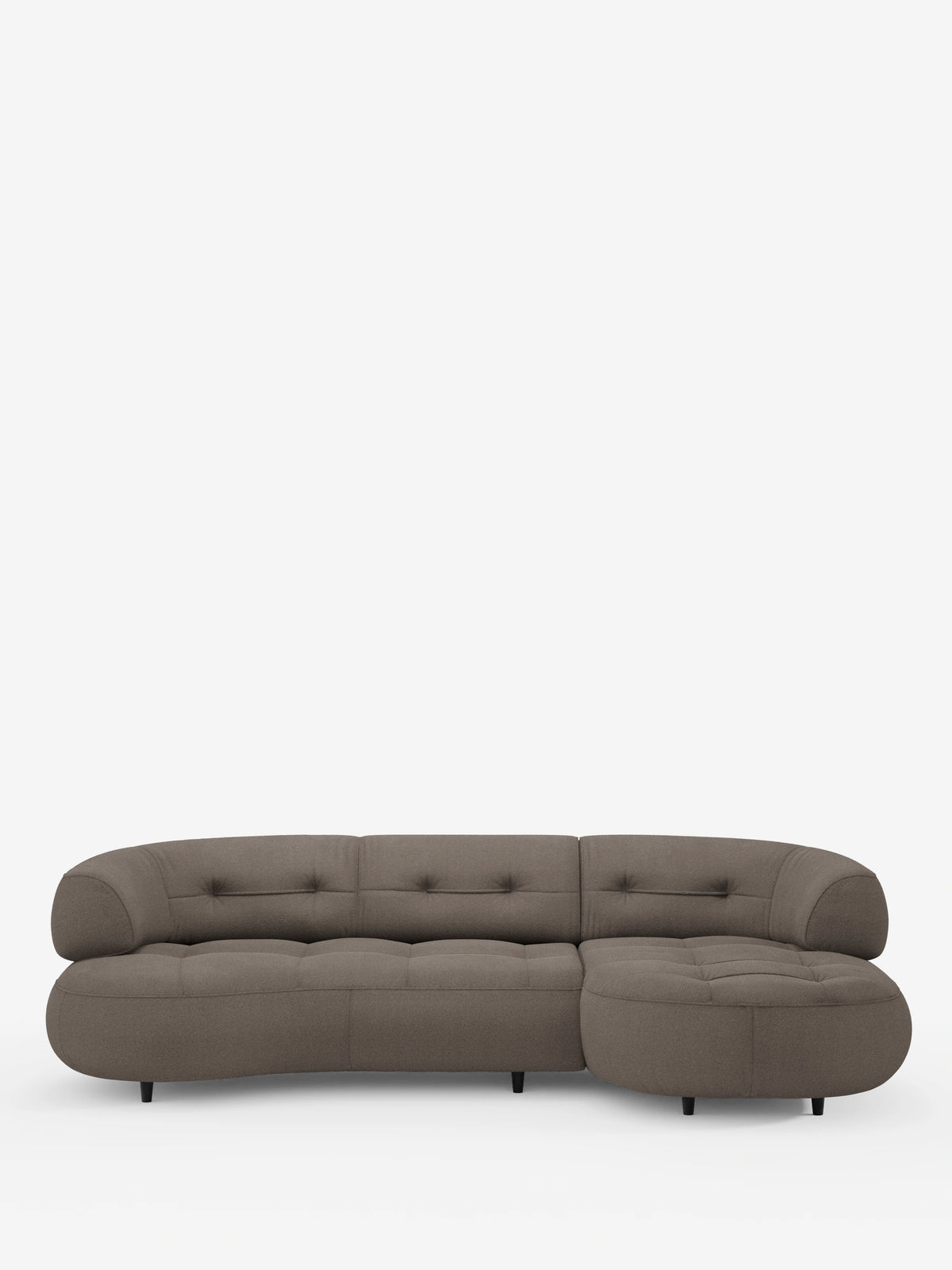 Un divano angolare Croissant dalla forma ricurva a fagiolo, con schienali scorrevoli in morbido tessuto effetto cotone smacchiabile T33 color taupe, si staglia su uno sfondo bianco con cuscini trapuntati e gambe corte e scure di forma cilindrica.