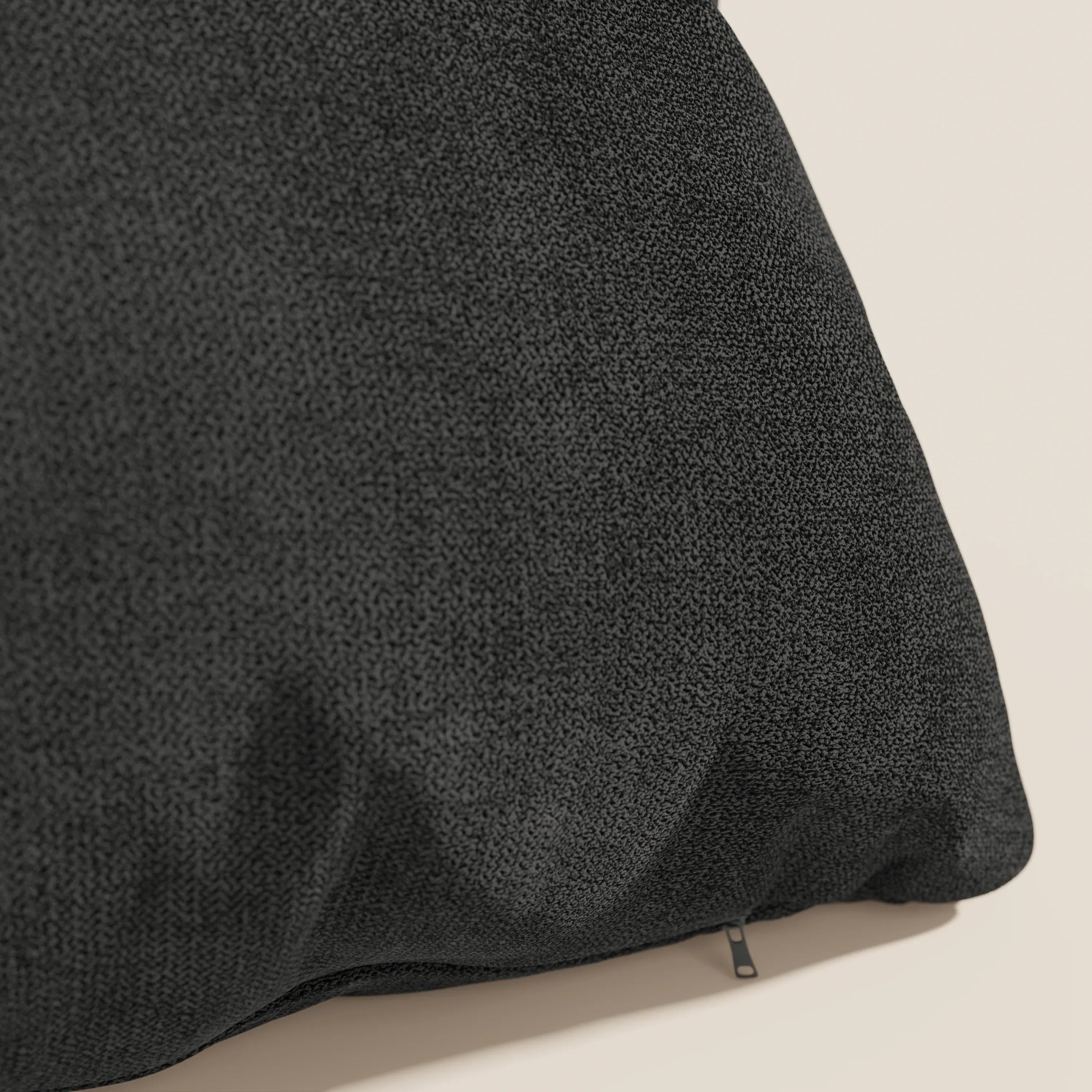 Primo piano del cuscino Destiny 45x45 cm di Divani.Store in tessuto morbido impermeabile T02 nero, con una sottile trama intrecciata e rivestimento lavabile. Il cuscino appare morbido con una cerniera visibile su una superficie chiara.