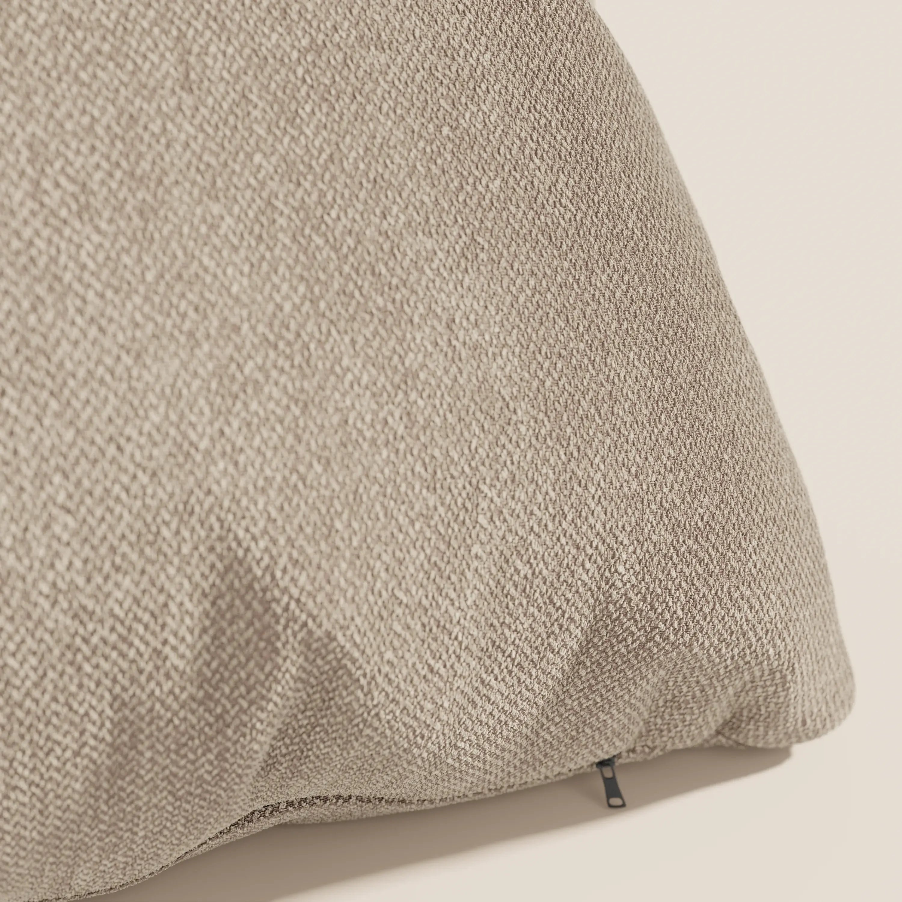 Primo piano del cuscino Sogno di Divani.Store in tessuto morbido smacchiabile T05 beige, caratterizzato da un raffinato motivo a intreccio e da una piccola cerniera nera all'angolo, ideale per cuscini eleganti.