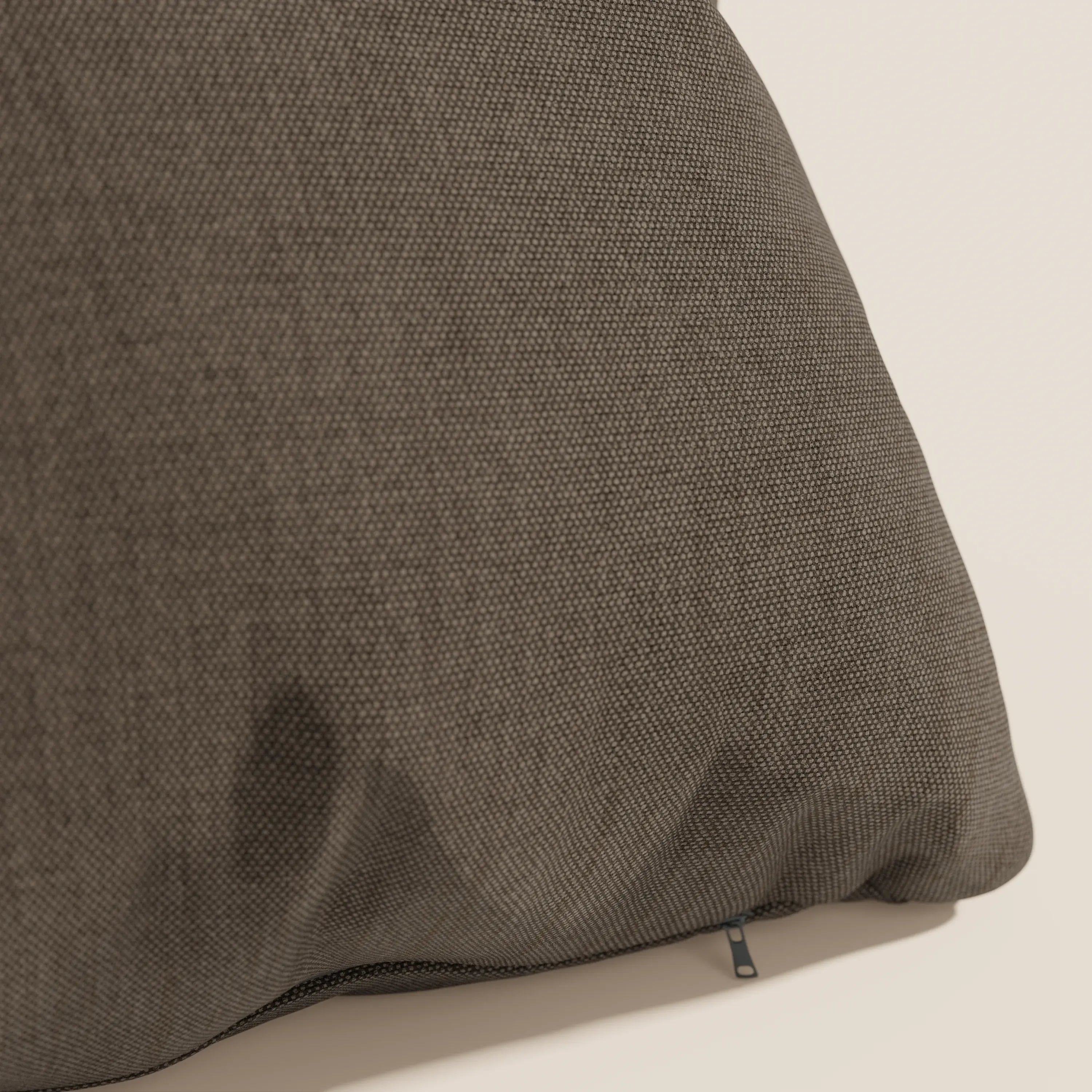 Primo piano del cuscino Honey 45x45 cm di Divani.Store in tessuto marrone simil cotone impermeabile T13, con una cerniera visibile su una cucitura e una sottile macchia più scura in basso a sinistra, su uno sfondo bianco sporco.