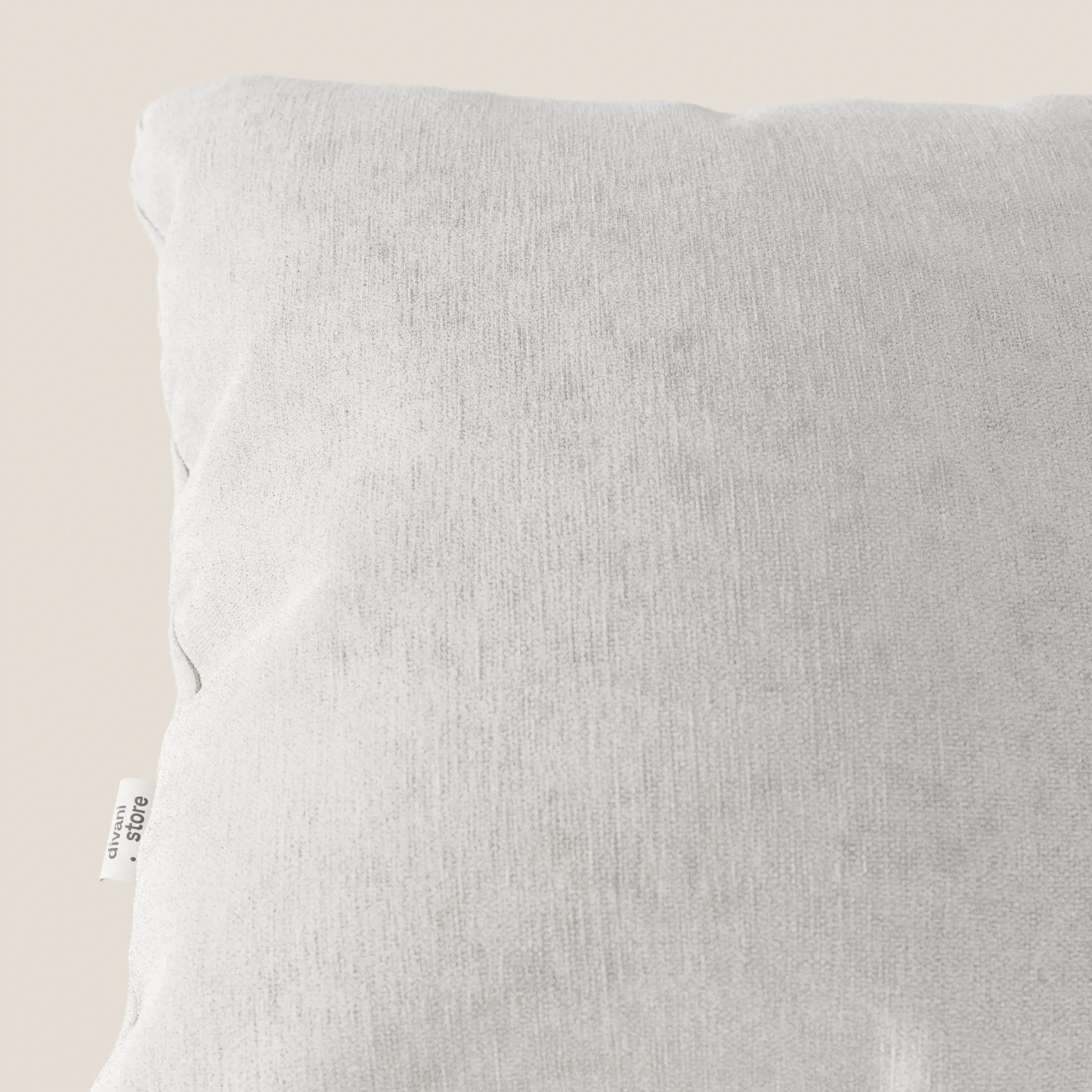 Primo piano del cuscino Bolero di Divani.Store, nel colore grigio chiaro con una texture sottile. Realizzato in morbido tessuto T31, resistente alle macchie, impermeabile e non restringibile. Una piccola etichetta bianca appare sul bordo sinistro su uno sfondo beige.
