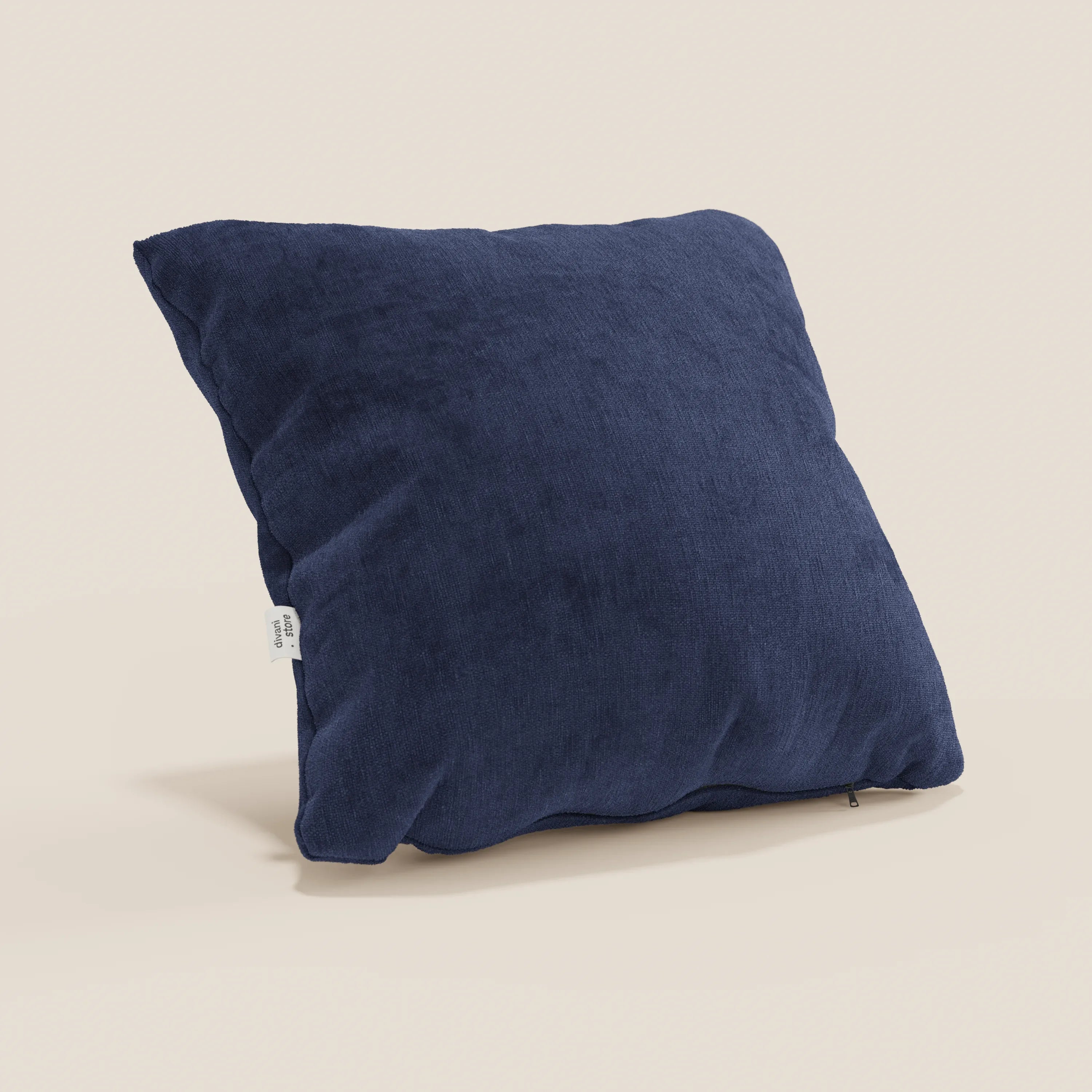 Il cuscino Bolero di Divani.Store, qui in blu scuro con tessuto morbido T31 resistente alle macchie, impermeabile e irrestringibile, è quadrato e presenta un'etichetta bianca laterale. Sullo sfondo c'è una parete beige chiara.