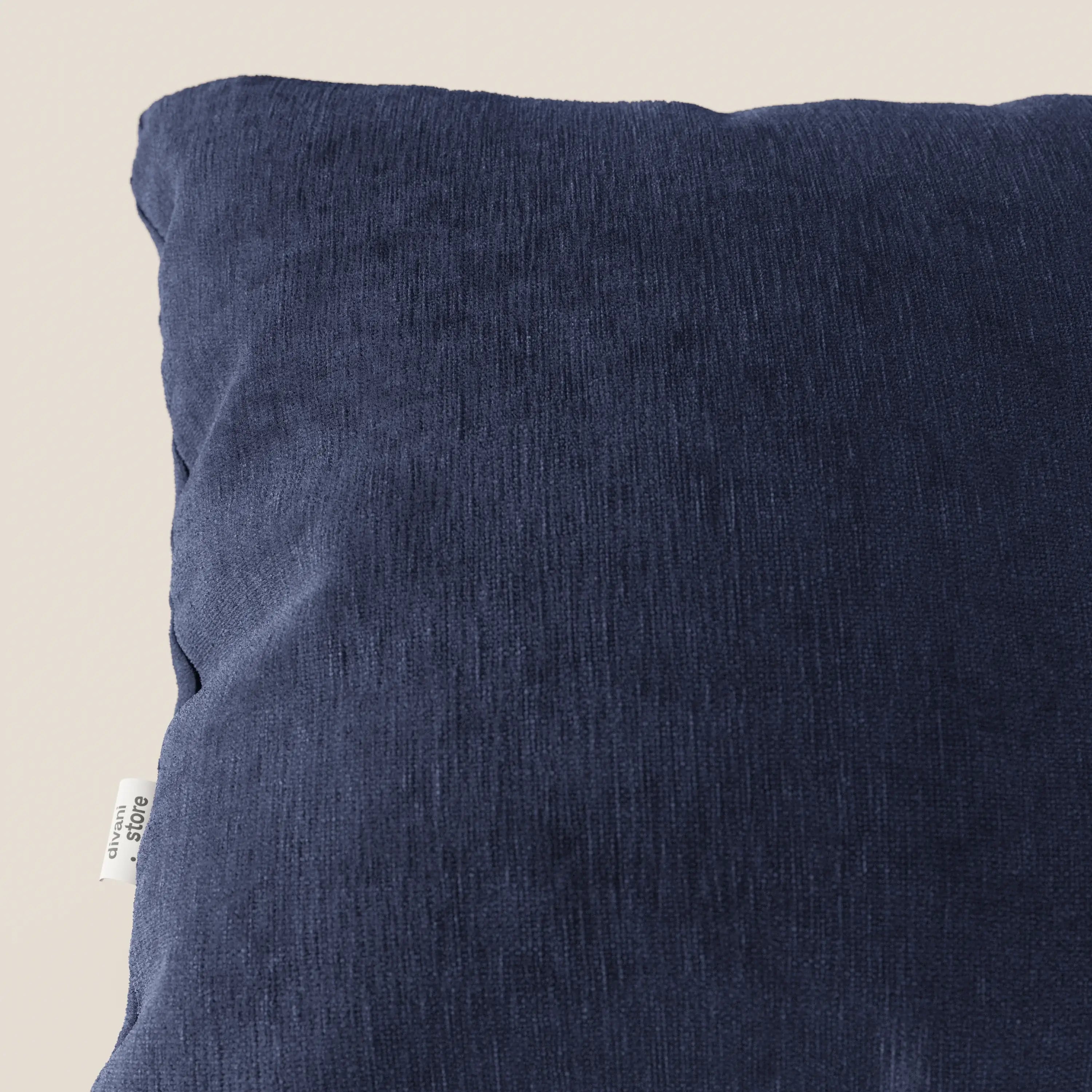 Primo piano del cuscino Bolero di Divani.Store in blu navy, realizzato in morbido tessuto T31 antimacchia, impermeabile e non restringente. Il cuscino presenta leggere rughe e una piccola etichetta bianca; lo sfondo è chiaro e neutro.