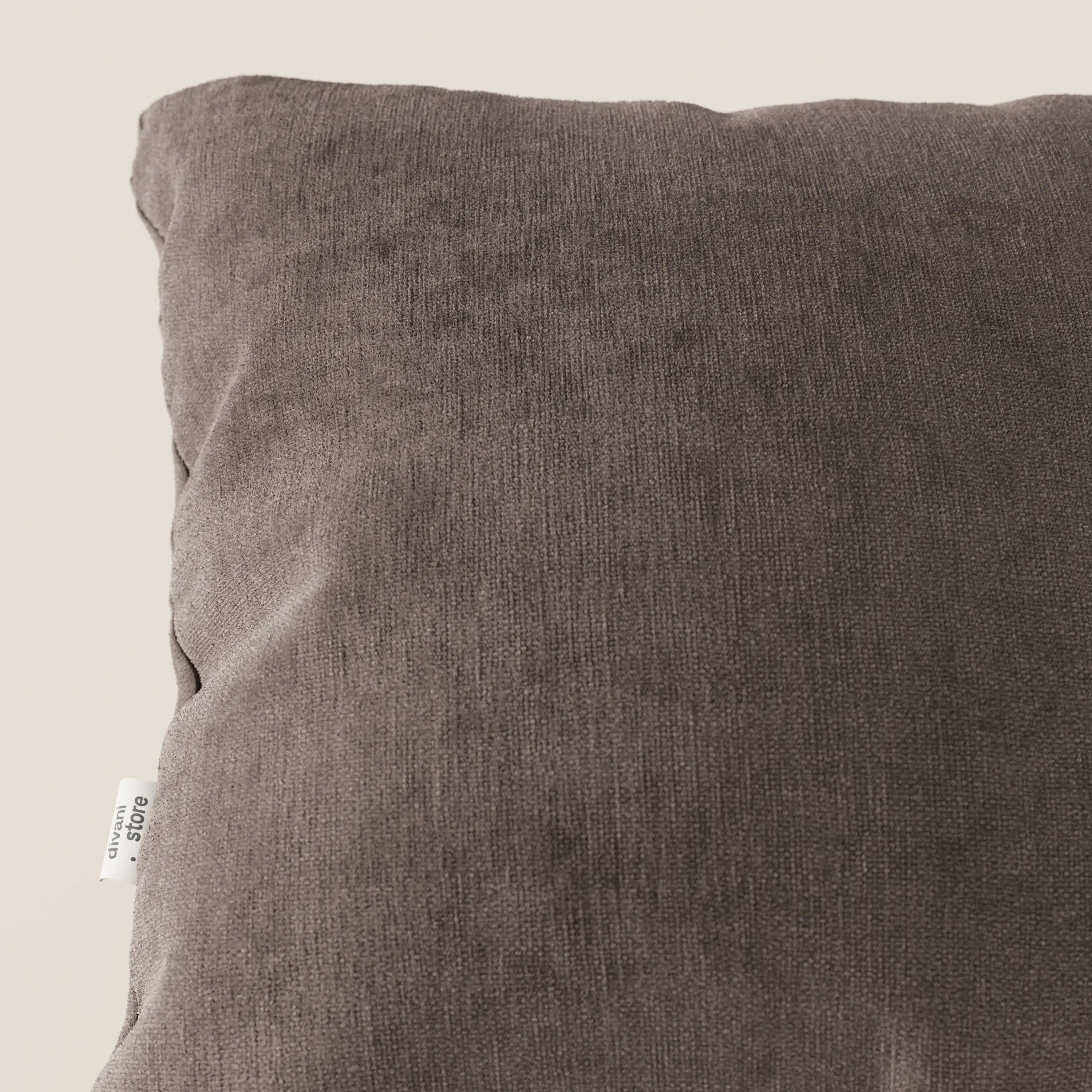 Primo piano di Bolero cuscino di Divani.Store, in tessuto T31 marrone scuro, morbido, antimacchia, impermeabile e non restringente. L'immagine mostra l'angolo superiore sinistro con l'etichetta bianca su uno sfondo beige chiaro.