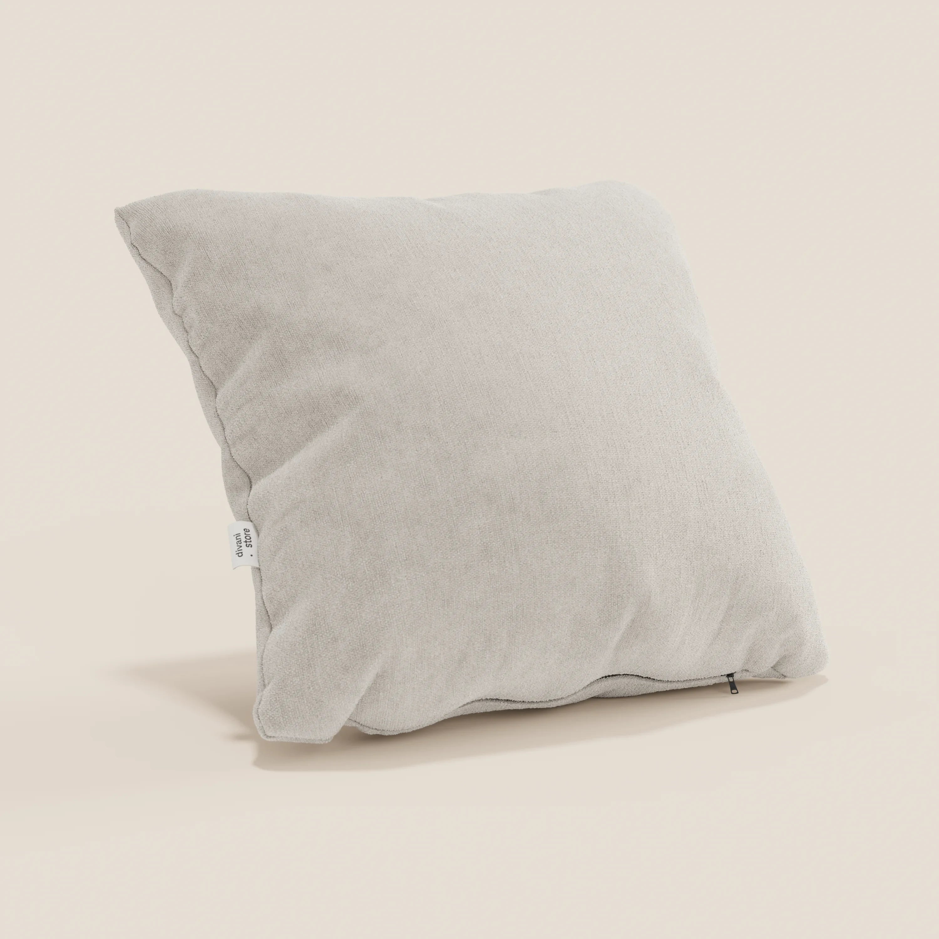 Un cuscino Bolero grigio chiaro di Divani.Store, quadrato e leggermente gonfio con una sottile texture, poggia ad angolo su uno sfondo beige. Presenta una piccola etichetta in tessuto bianco e una cerniera lungo il bordo inferiore. Realizzato in tessuto T31 lavabile e impermeabile.