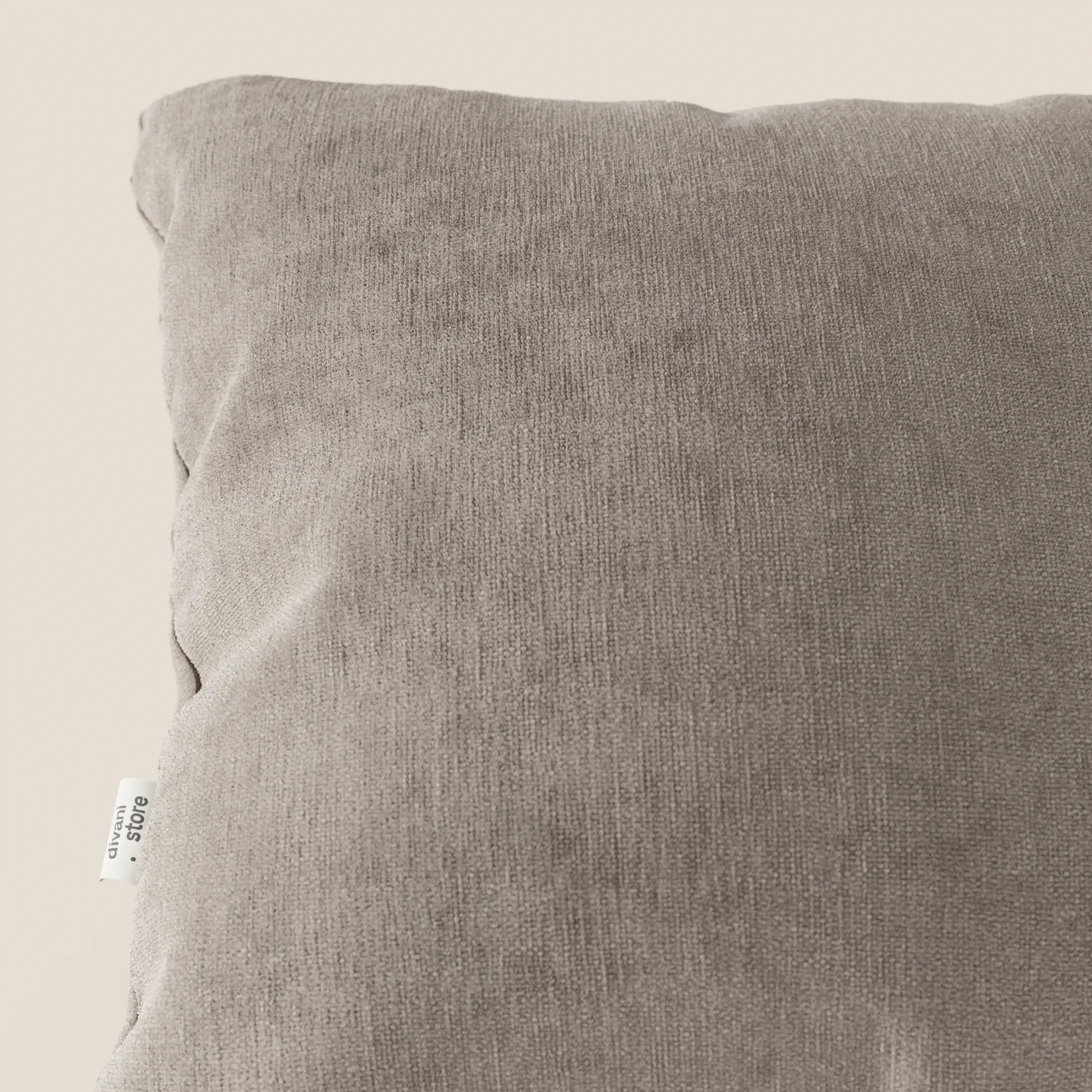 Primo piano dell'angolo superiore sinistro di Bolero cuscino di Divani.Store in morbido, smacchiabile, impermeabile e irrestringibile tessuto T31, con etichetta in tessuto visibile sulla cucitura. Lo sfondo è un semplice beige chiaro. Viene mostrata solo una parte del cuscino.